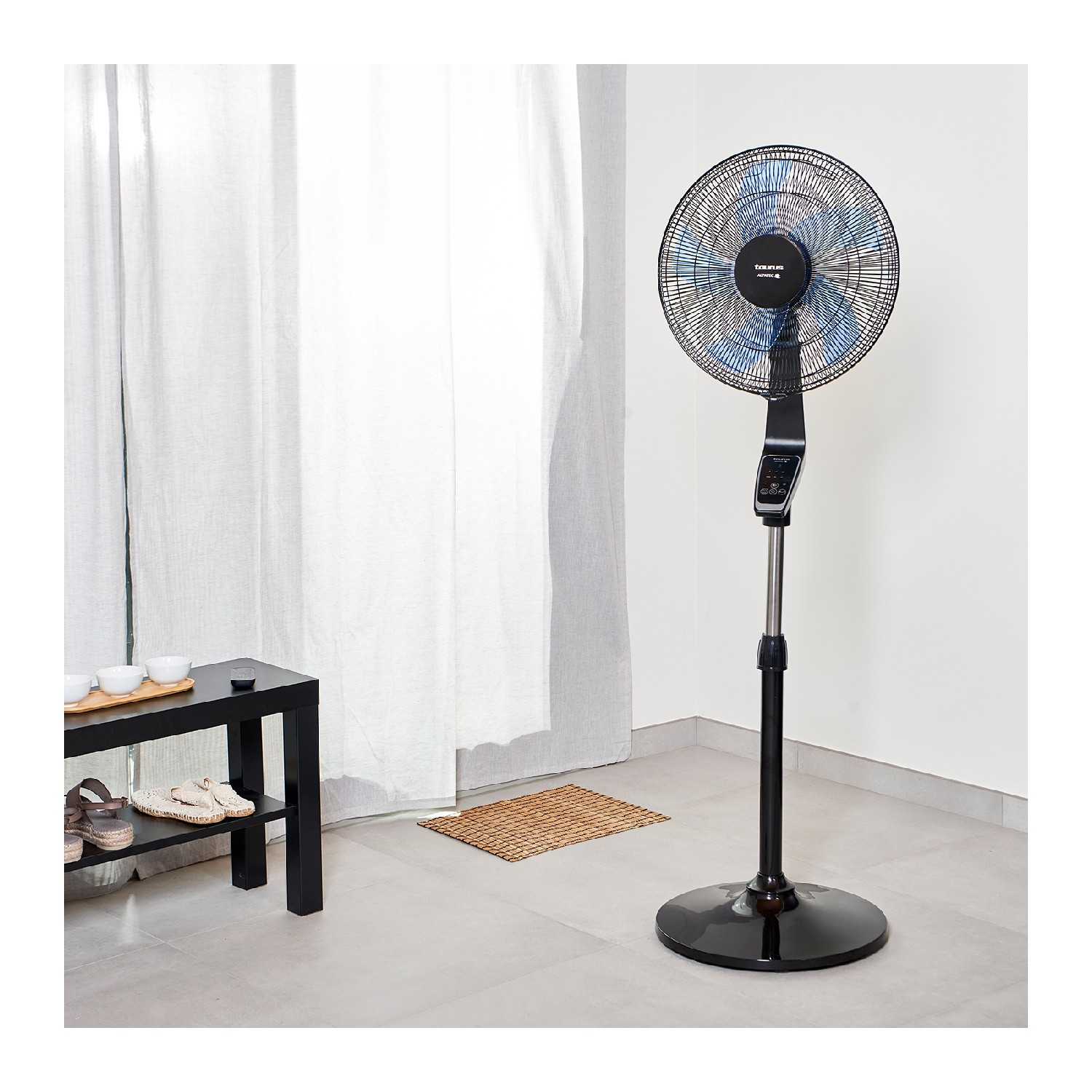 Ventilador de pie negro y plateado con mando a distancia, cerca de una mesa negra.