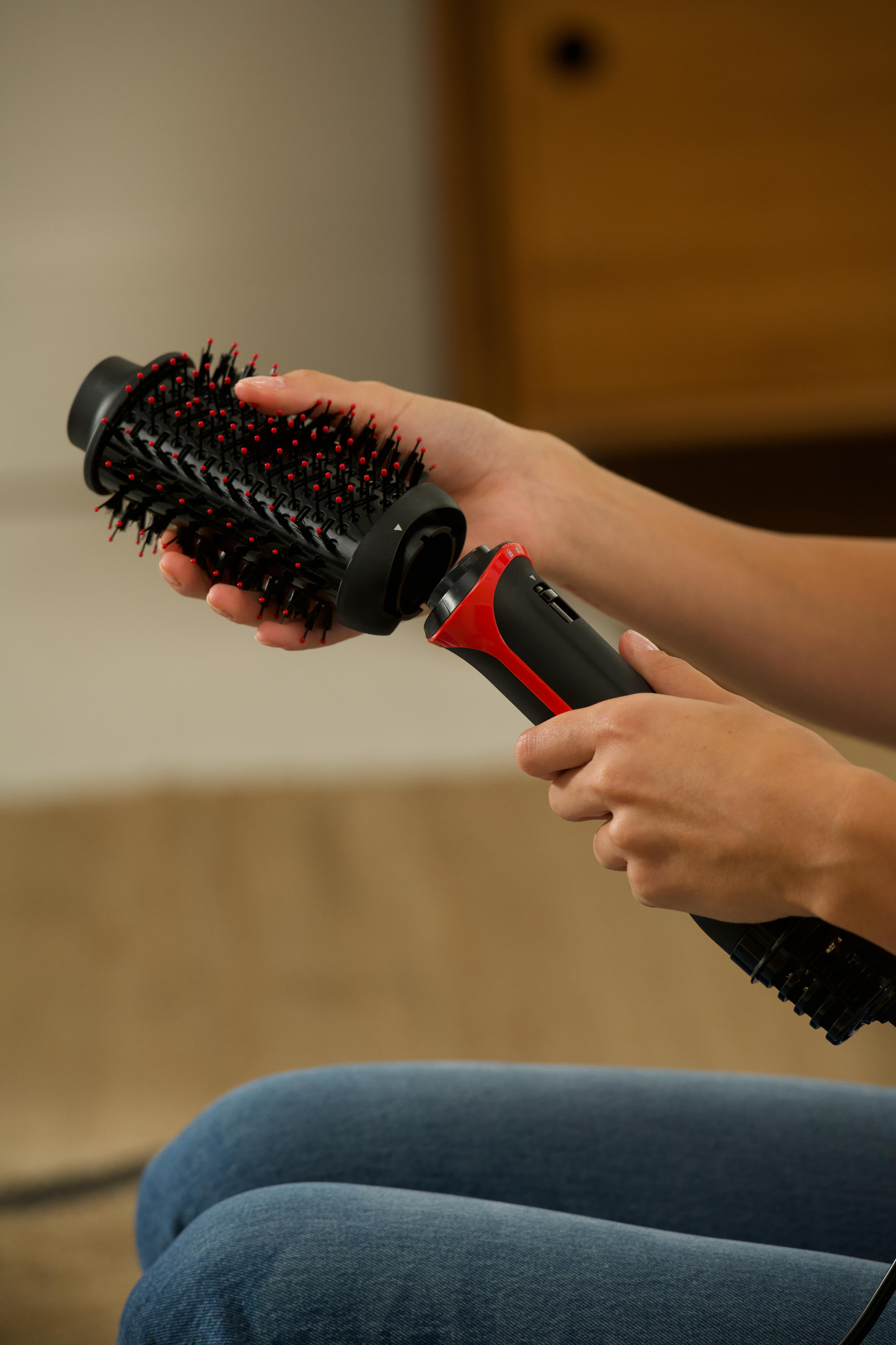 Hände halten eine Haarbürste, der Bürstenkopf und der Griff sind getrennt.