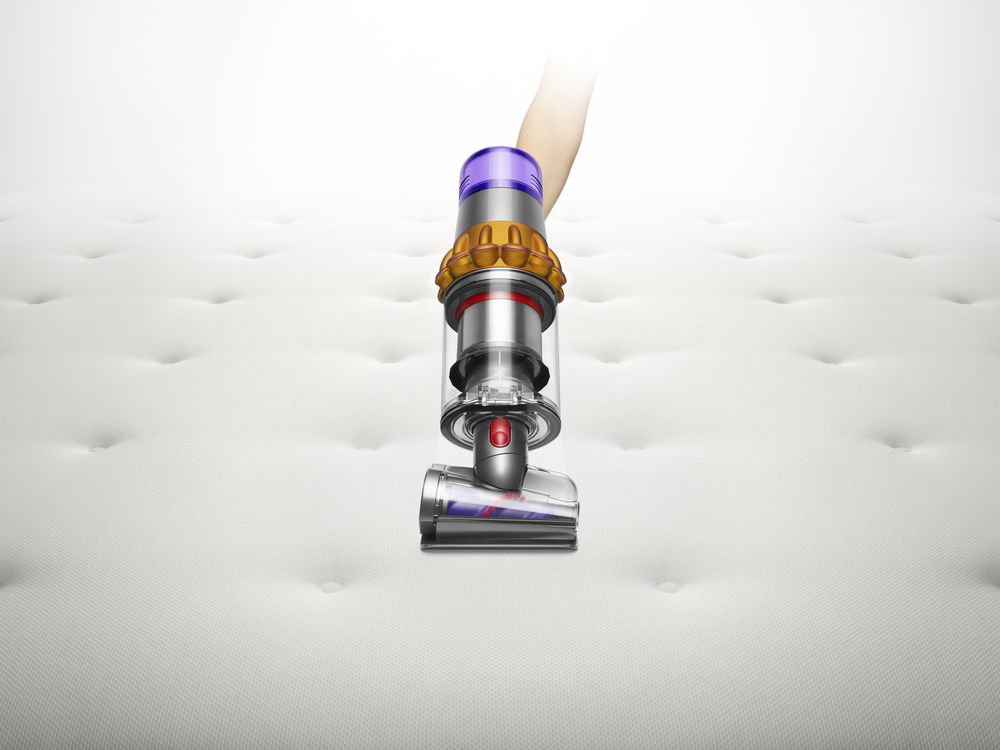 Een Dyson stofzuigerkop die een wit gewatteerd matras schoonmaakt. Een hand houdt de stofzuiger vast.