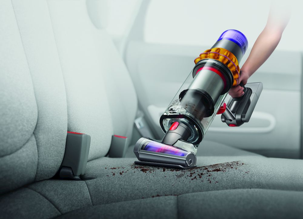 Een persoon die een Dyson stofzuiger gebruikt om een autostoel schoon te maken.
