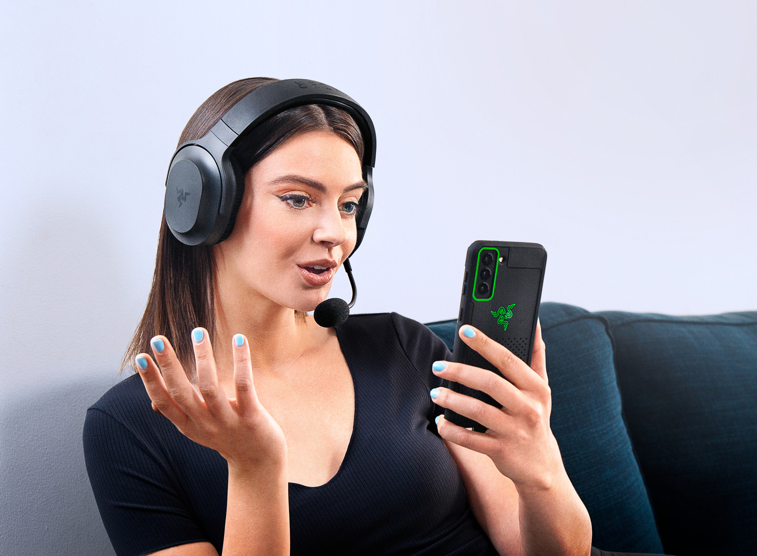 Donna con cuffie, tiene in mano il telefono, in videochiamata. Cuffie nere, telefono con logo Razer.