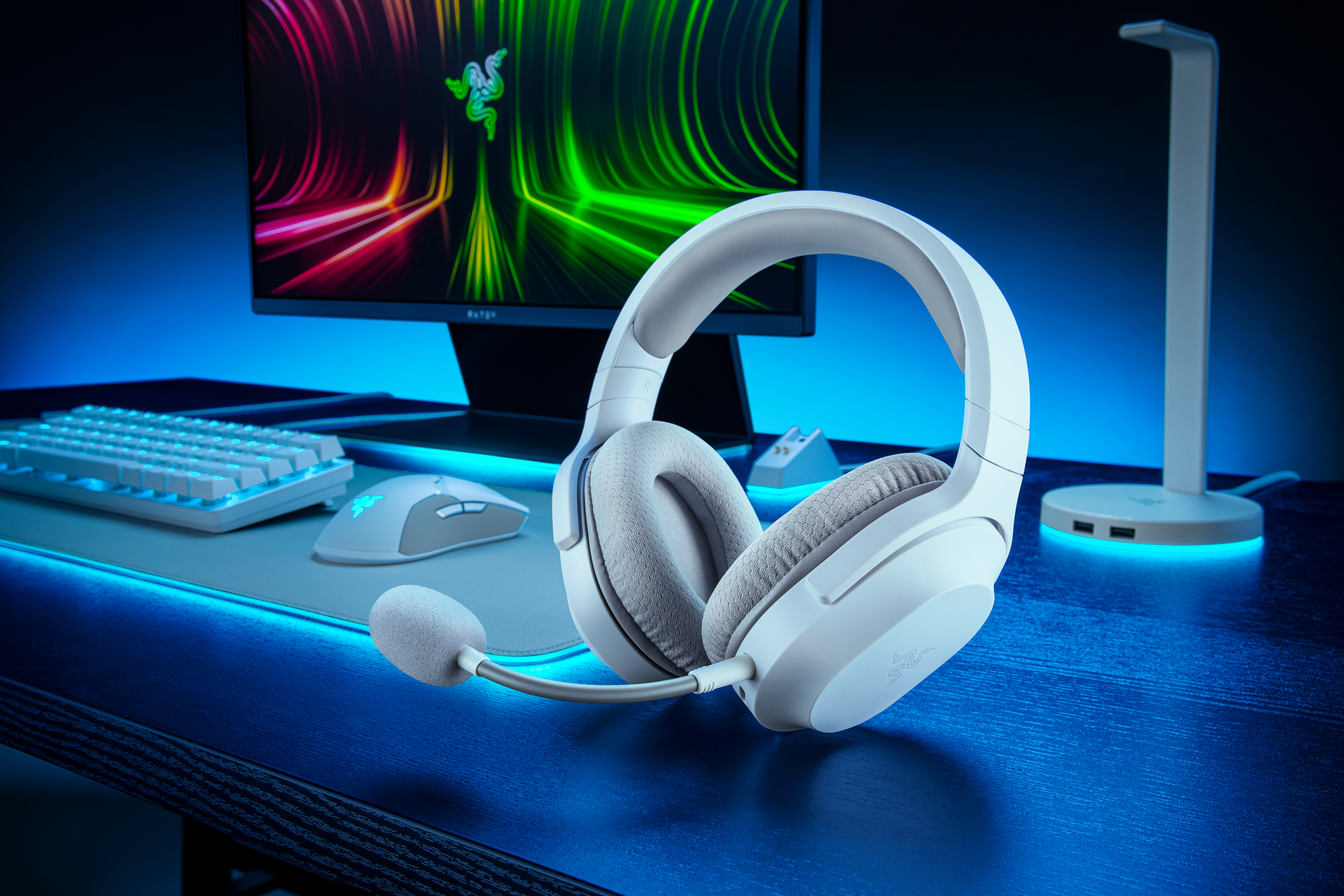 Weißes Gaming-Headset, Mikrofon ausgefahren, auf einem Schreibtisch mit Tastatur, Maus und Monitor, blaues Licht.