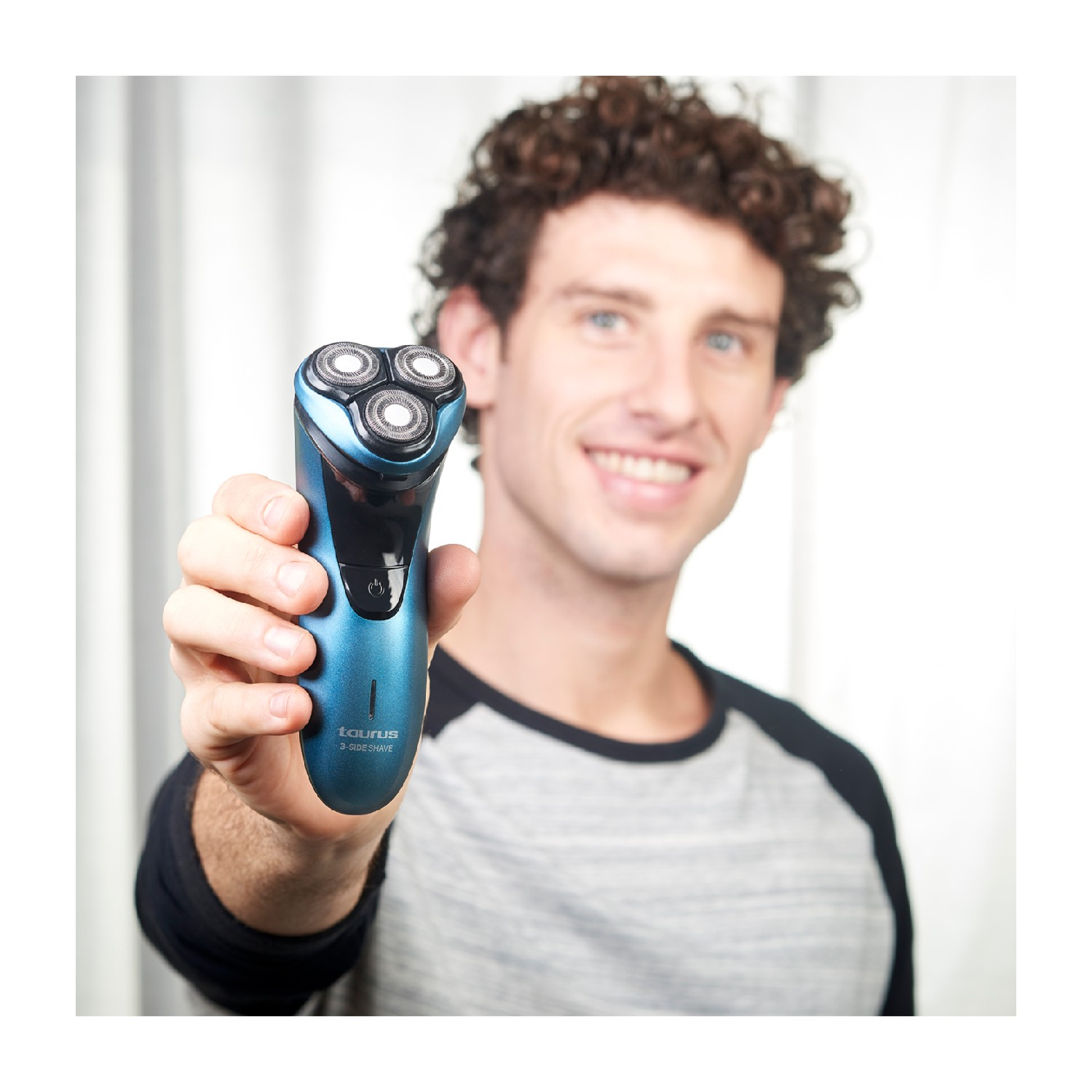 Un hombre sostiene una afeitadora eléctrica azul, sonriendo. La afeitadora tiene tres cabezales.