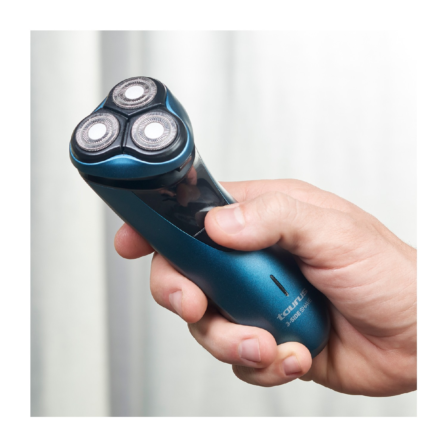 Mano de hombre sosteniendo una afeitadora eléctrica azul y verde azulado. La afeitadora tiene tres cabezales.