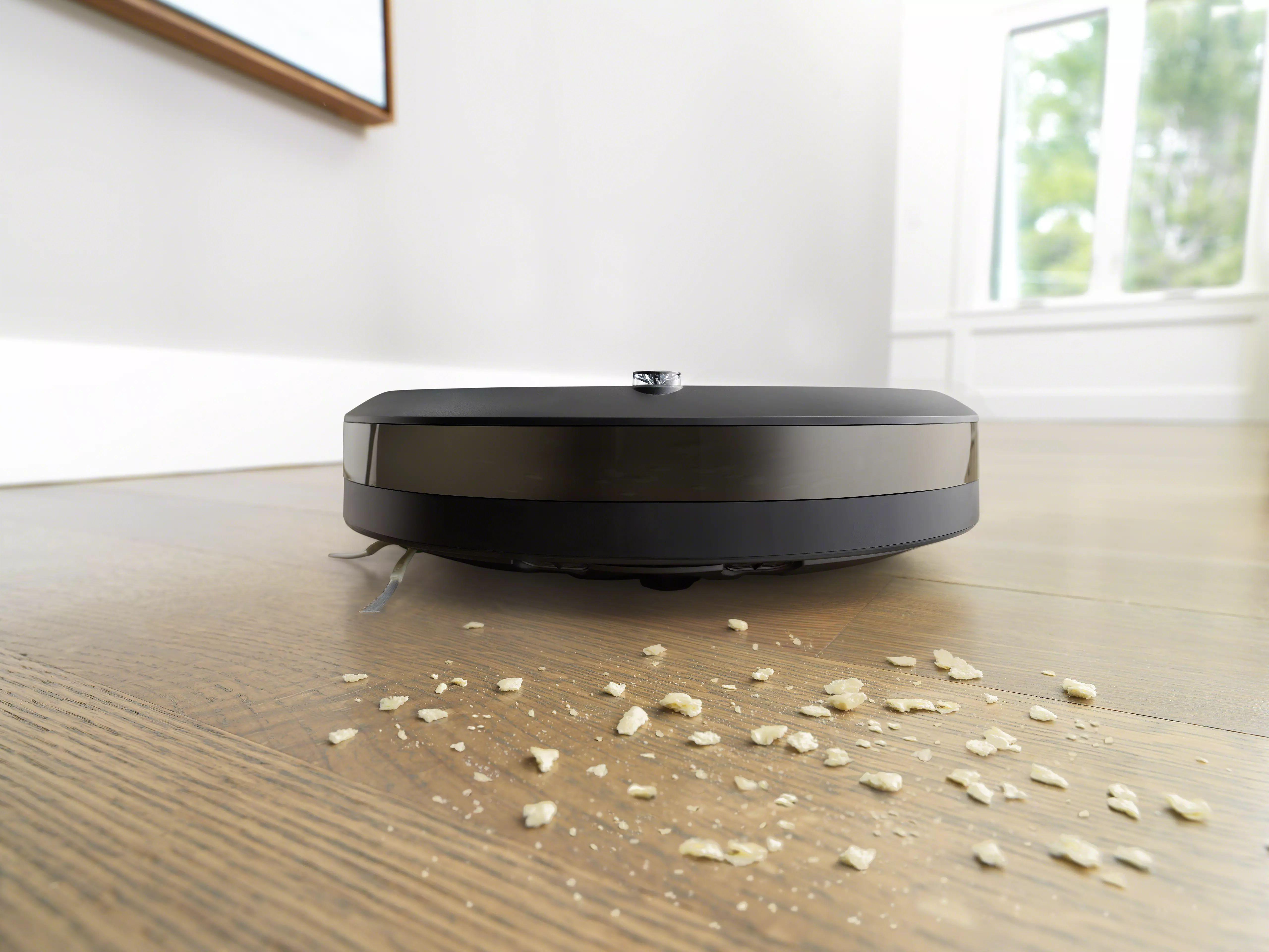 Roboter-Staubsauger reinigt einen Holzboden, um den herum sich Schmutz verteilt.
