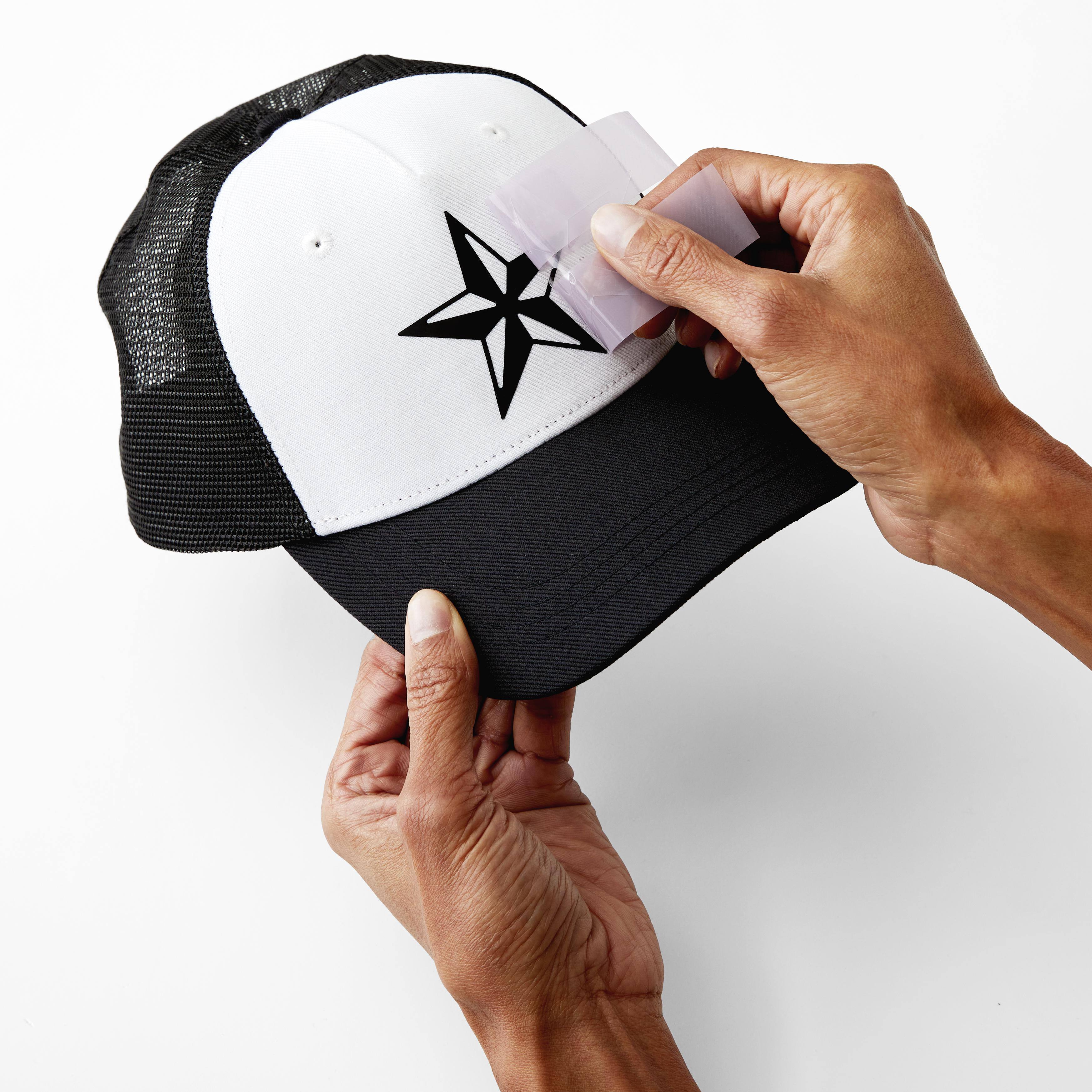 Eine Person, die einen sternförmigen Aufkleber auf eine schwarz-weiße Trucker-Mütze klebt. Weißer Hintergrund.