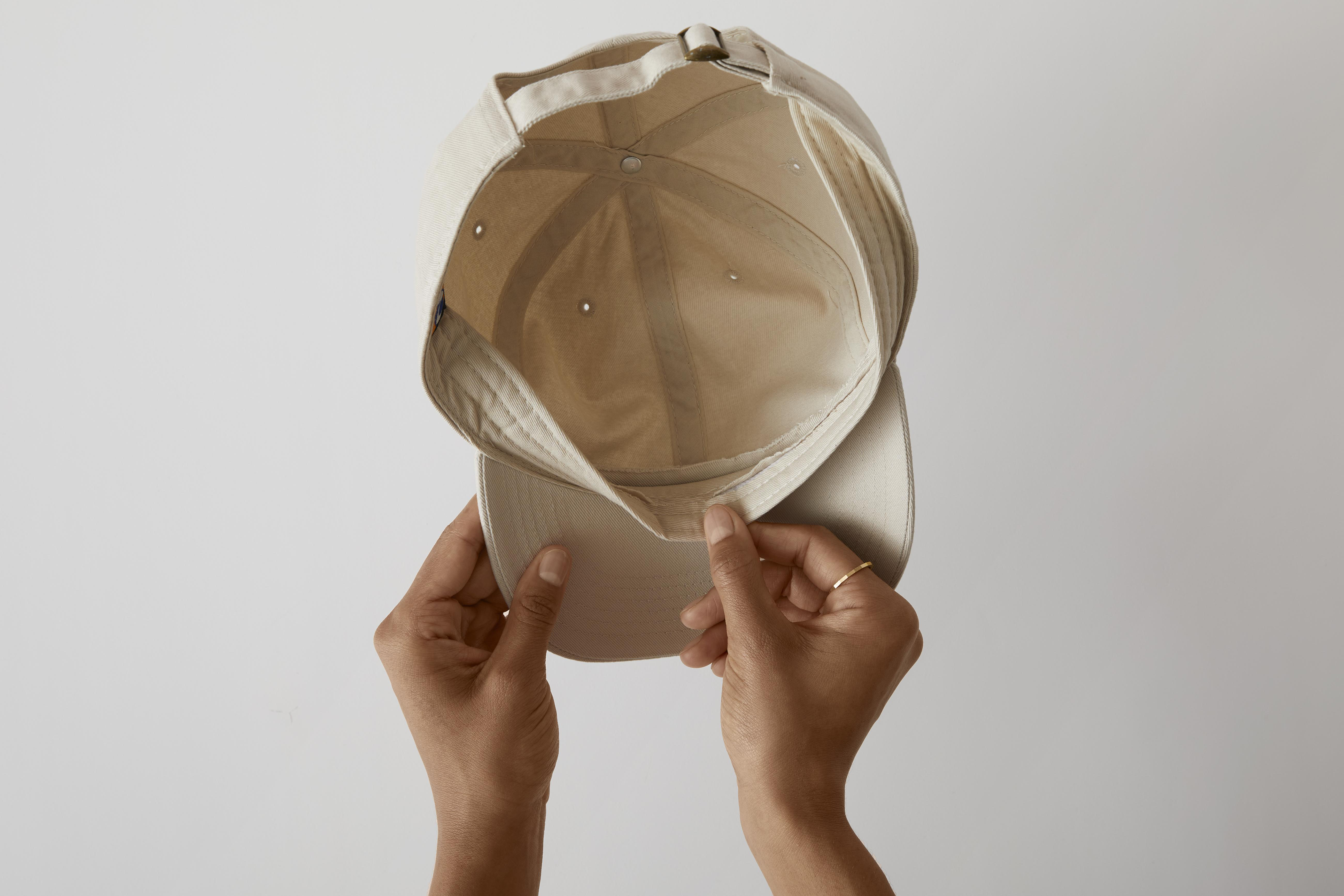 Hände halten eine beige Baseballkappe von oben.