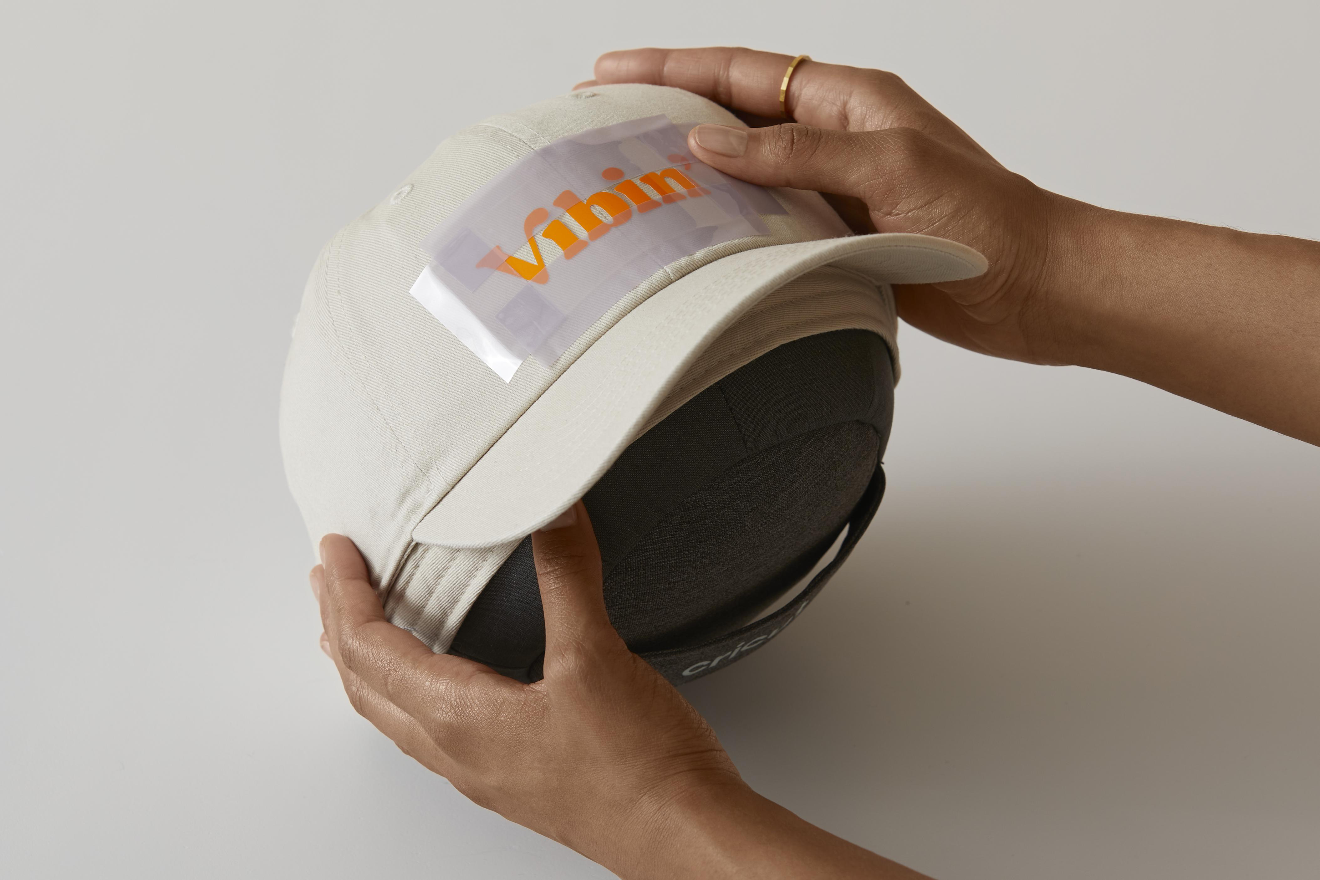 Hände halten eine Baseballkappe mit Vinyltransfer des Wortes 'Vibin'.