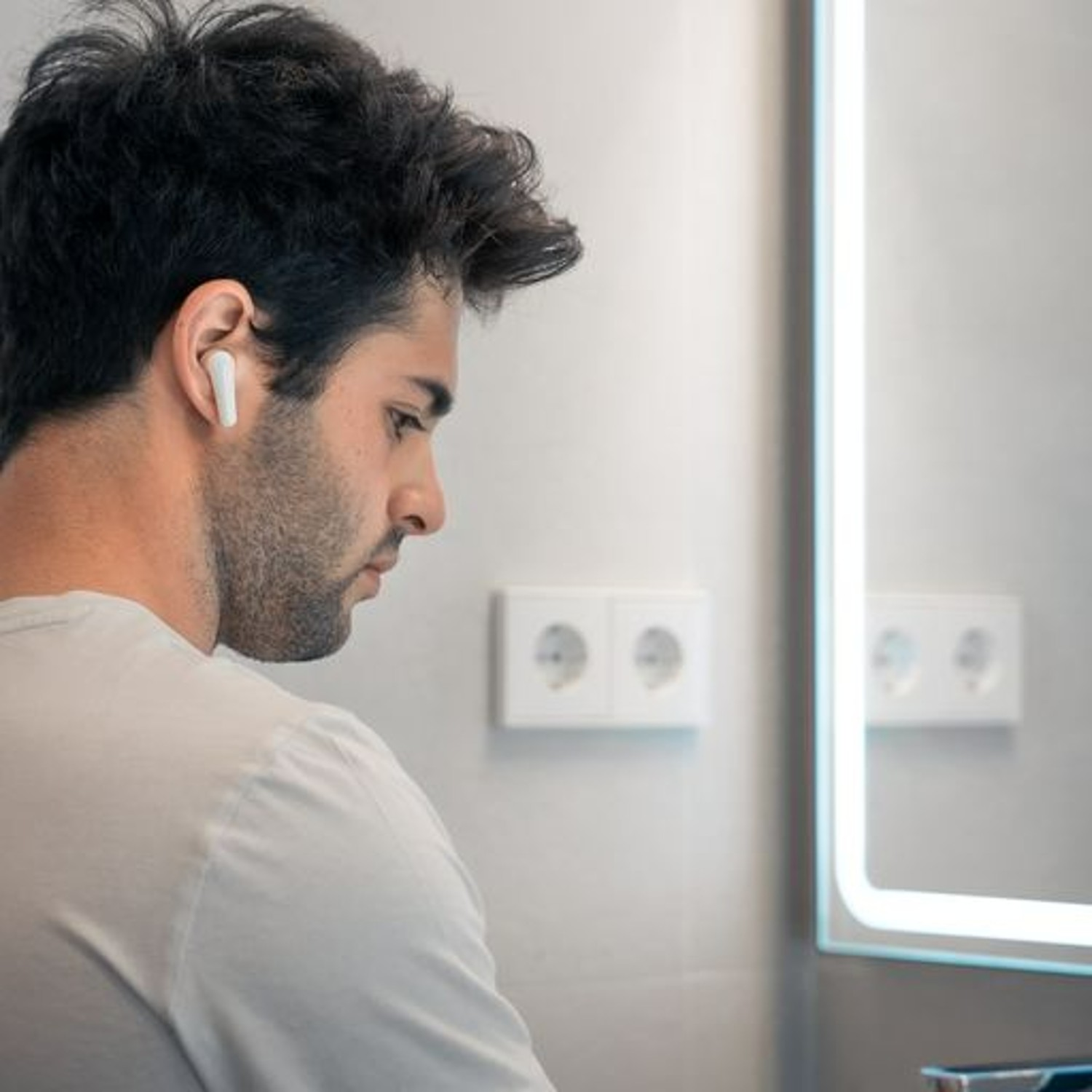 Hombre con auricular, mirando al espejo. Dos enchufes están detrás de él.
