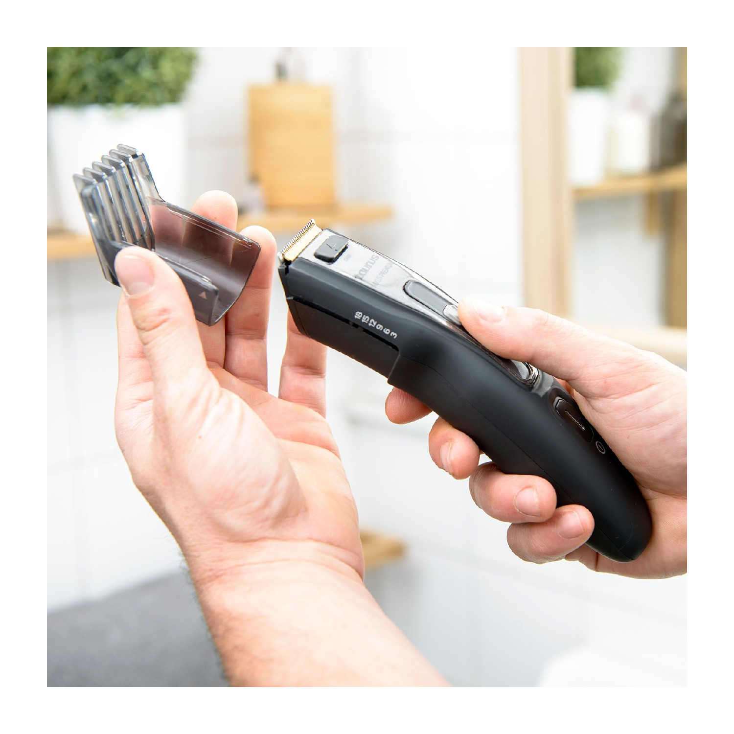 Mano mostrando una recortadora de cabello negra sin protector de cuchilla sobre blanco.