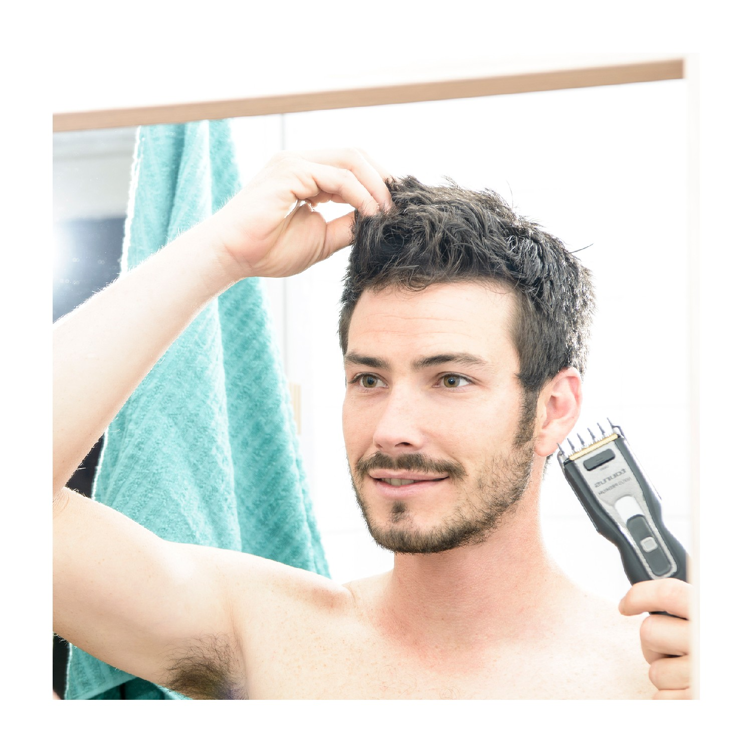 Hombre afeitándose la barba con una afeitadora eléctrica en un espejo. Está sin camisa.