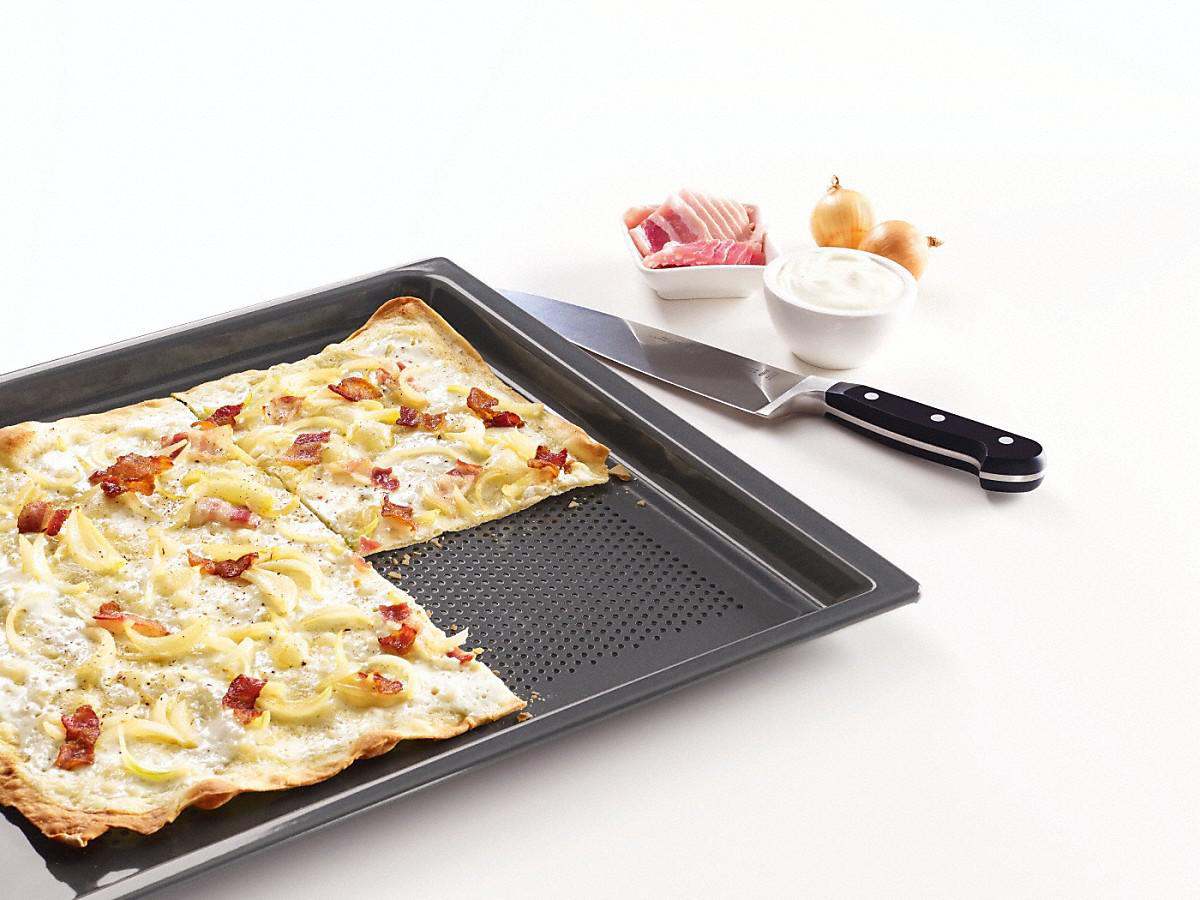 Pizza auf einem Backblech mit Speck, Zwiebeln und einem Messer.
