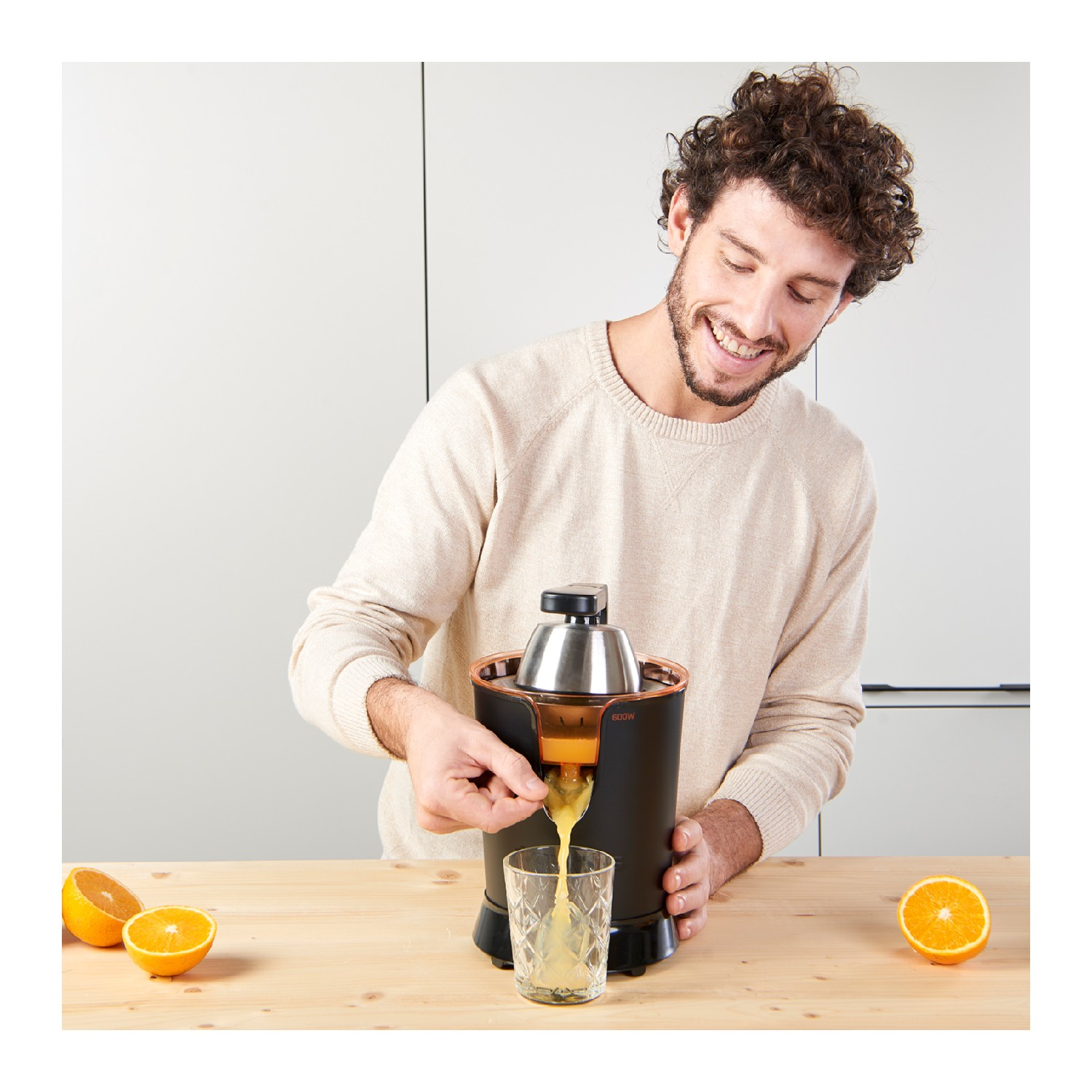 Hombre vertiendo jugo de naranja de una exprimidora en un vaso. Las naranjas están sobre la mesa de madera. Fondo blanco.