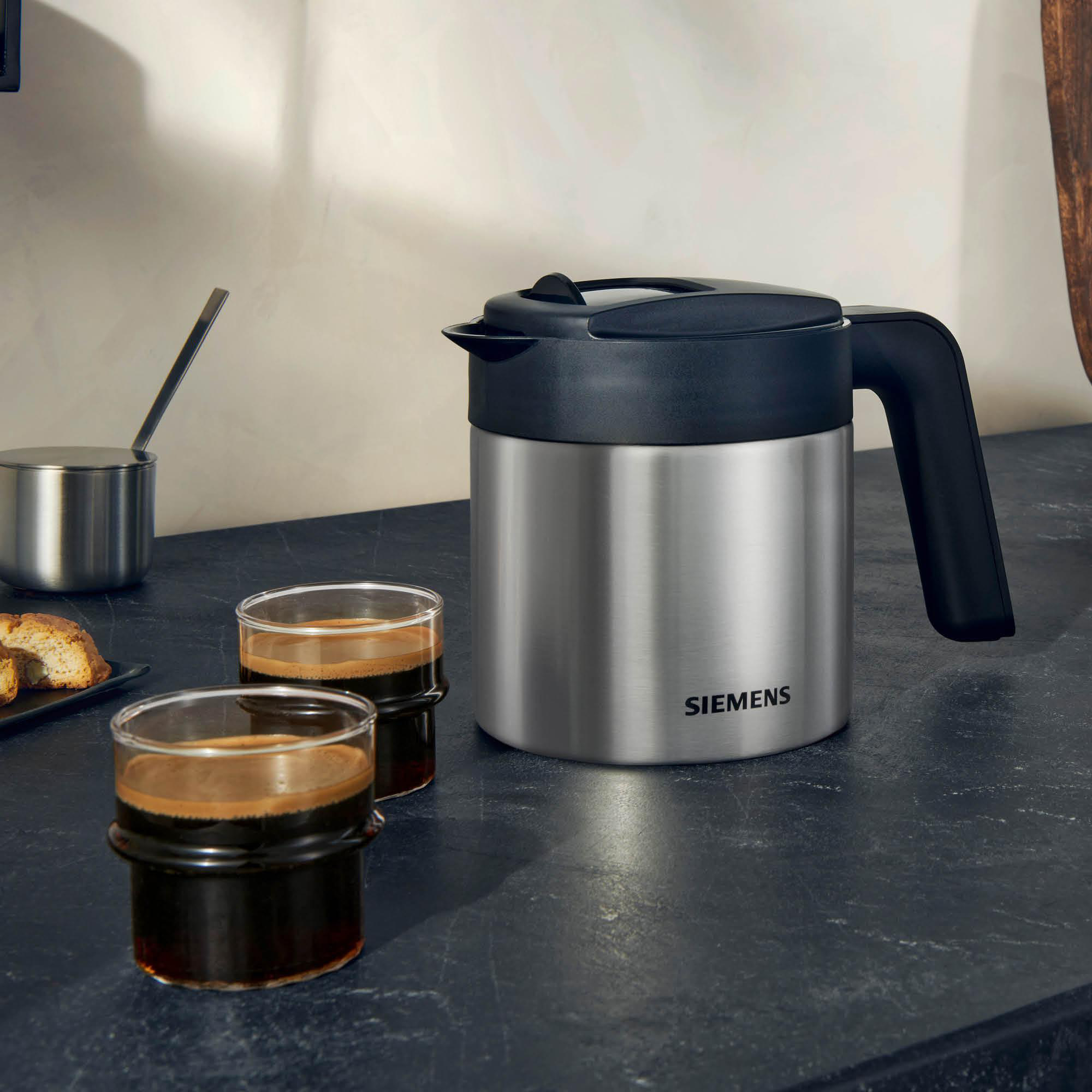 Eine Kaffeekanne aus Edelstahl mit zwei Kaffeegläsern auf einer Theke.