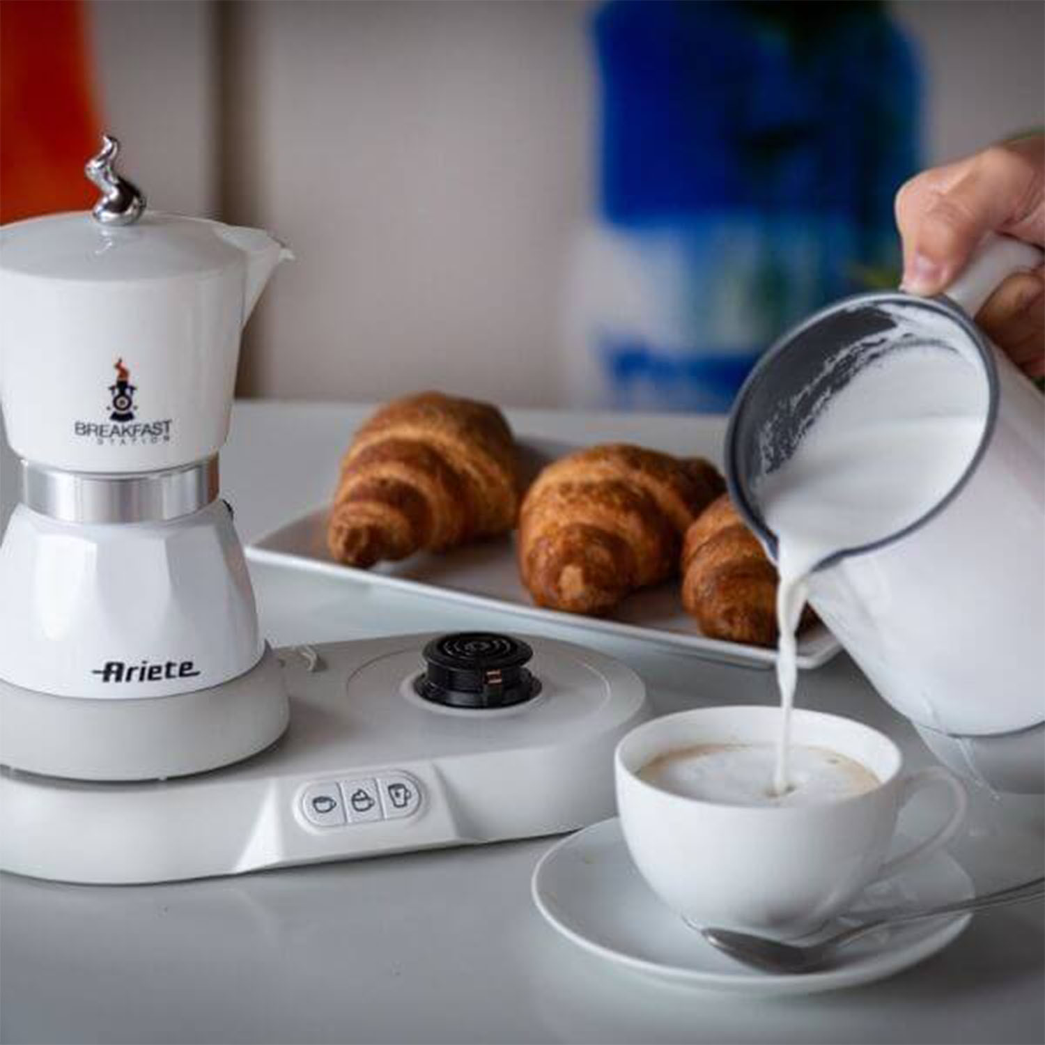 Latte versato in una tazza di caffè accanto a croissant e una caffettiera.