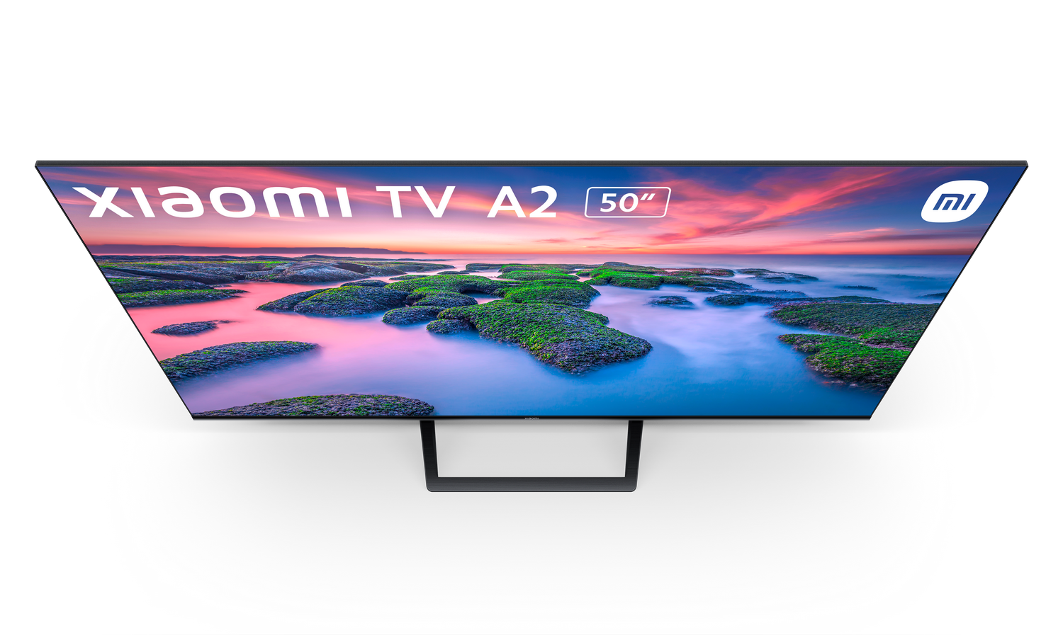 Pantalla Xiaomi TV A2 50" muestra un paisaje. Islas verdes en primer plano, cielo de fondo con colores de atardecer. Soporte negro.