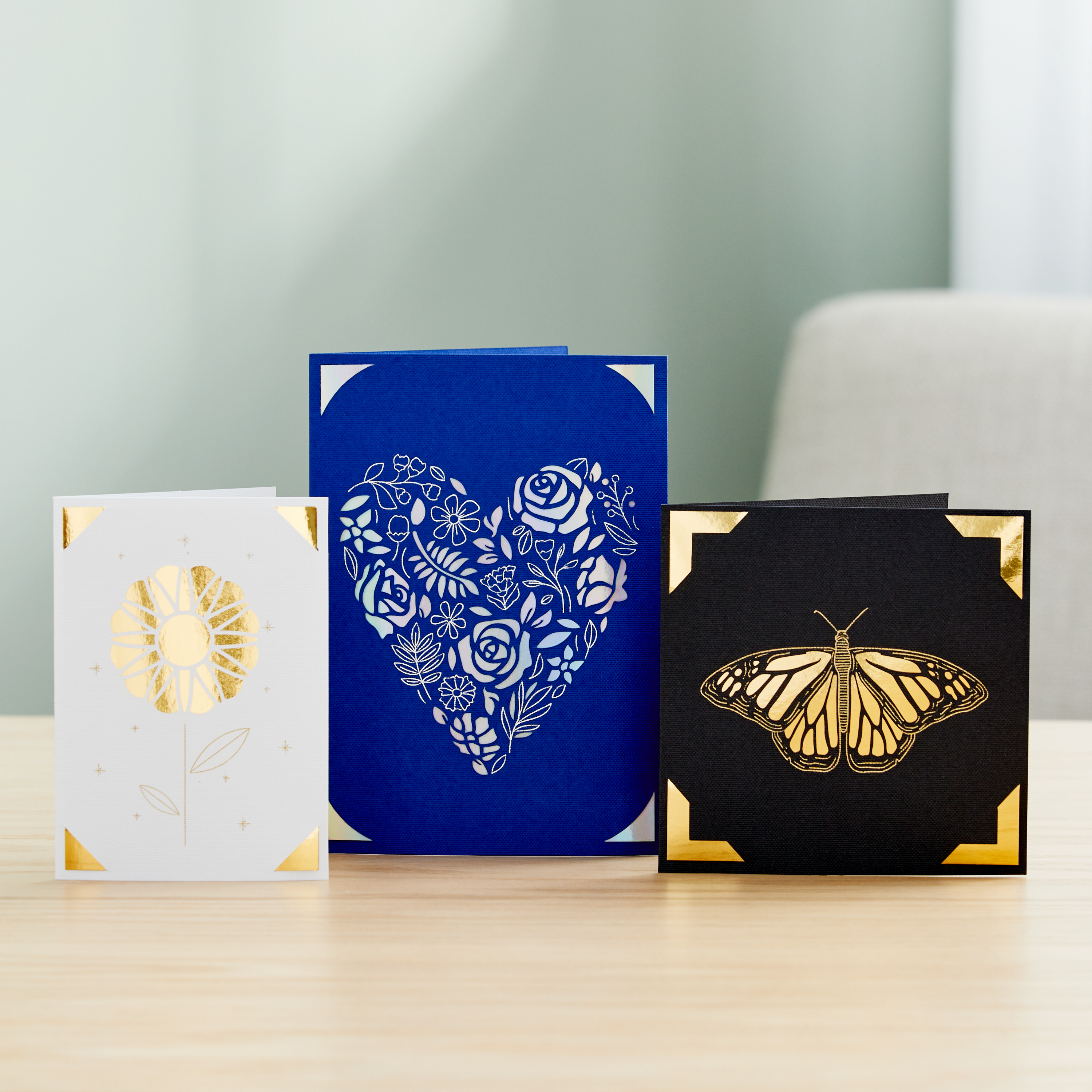 Drei Papierkarten mit Goldrändern, ein Blumen-, ein Herz- und ein Schmetterlingsdesign.