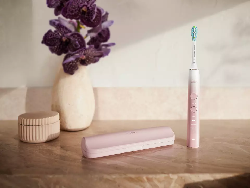 Pinke elektrische Zahnbürste, Etui und kleines Deko-Glas mit lila Blüten.