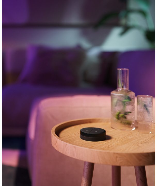 Black smart home controller on a wooden table. Glass vase and a glass are next to it. Blurred background.