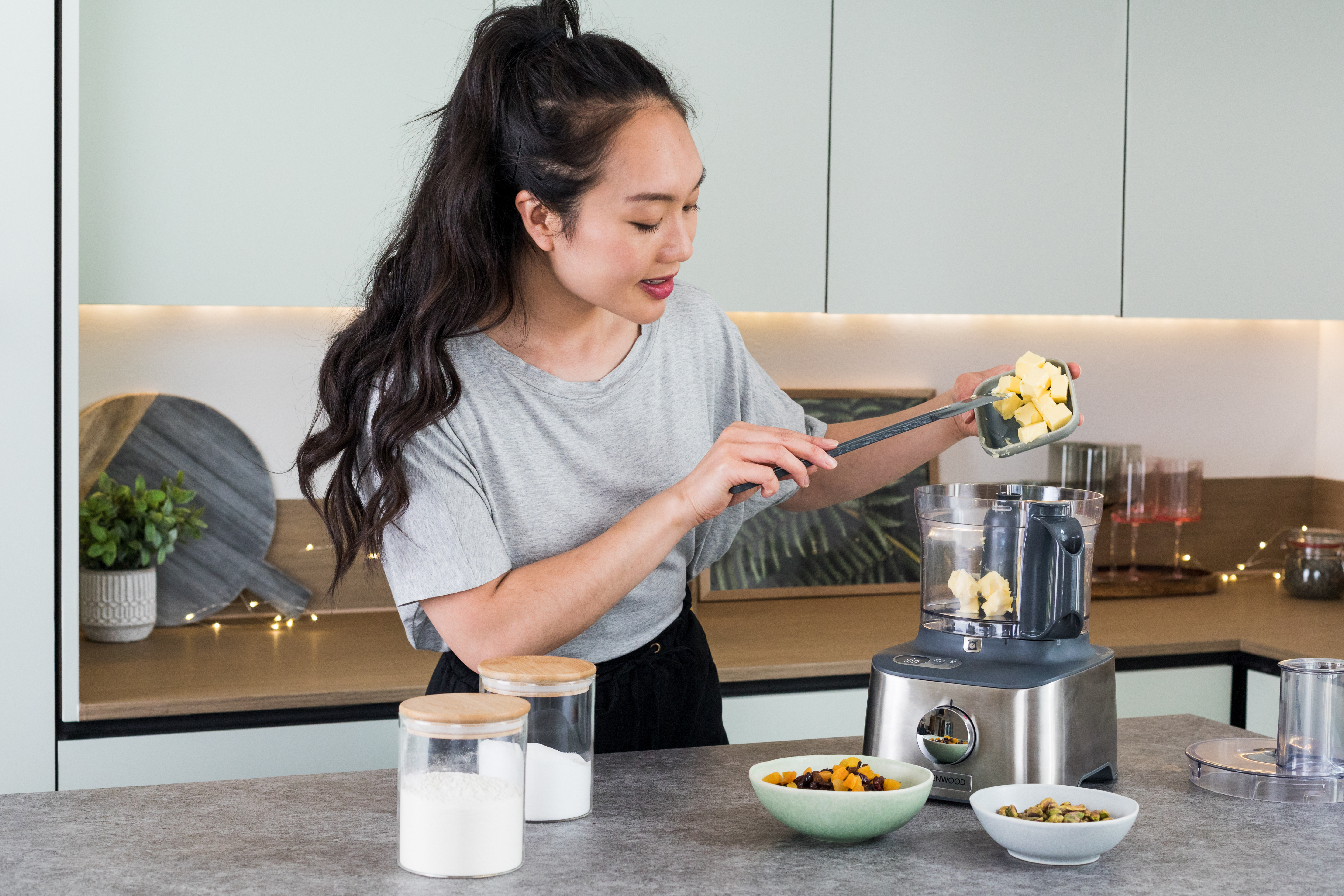 Woman adding ingredients to a food processor.  Other ingredients are visible.