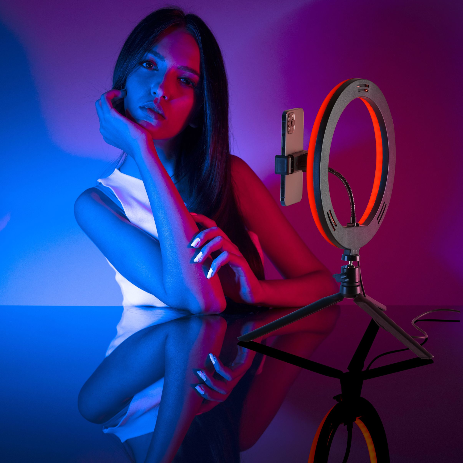 Woman with ring light and phone. Pink and blue background. Reflection on the surface.
