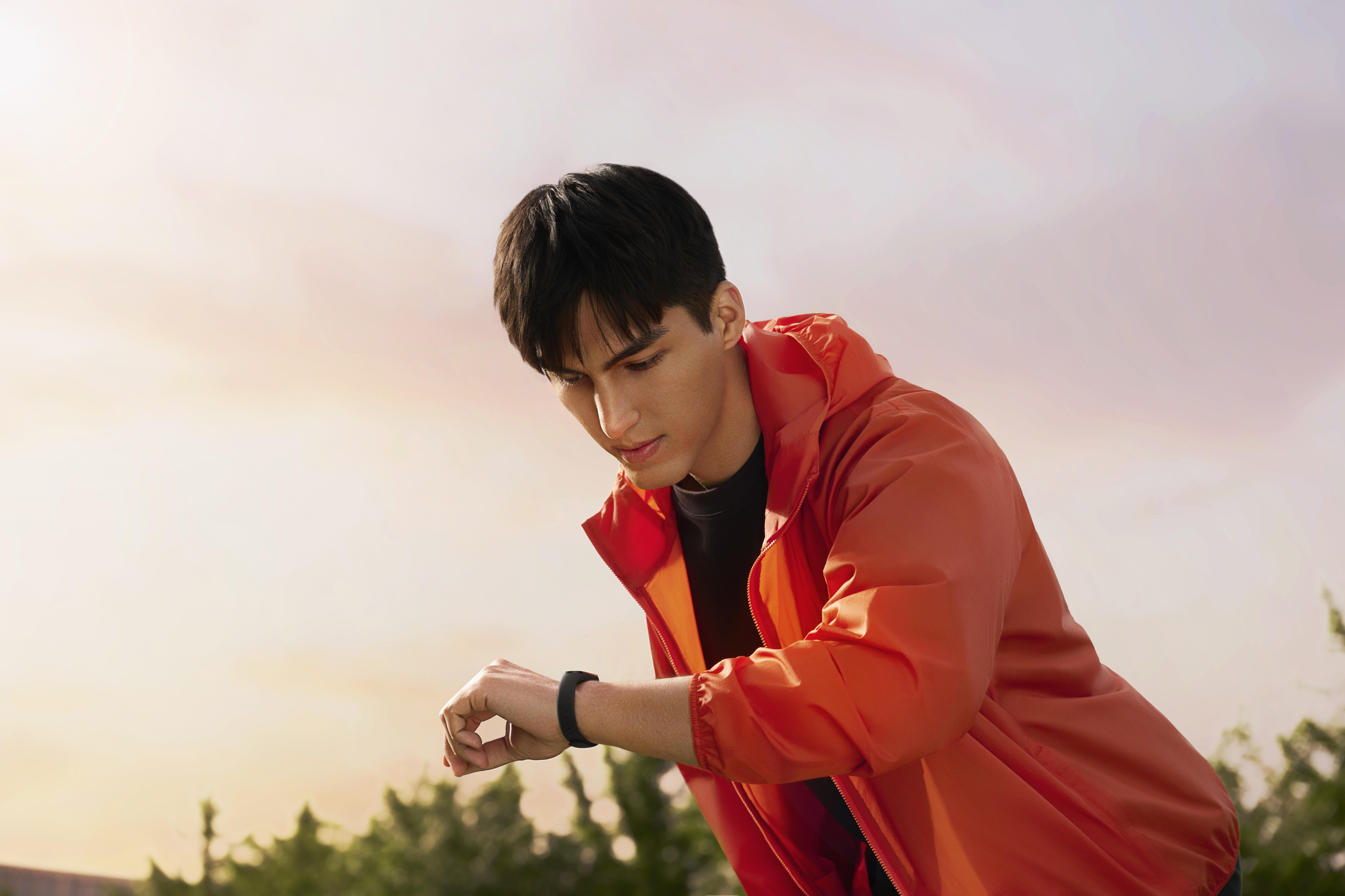 Mann mit Smartwatch. Ein Mann in orangefarbener Jacke checkt seine Smartwatch. Sonniger Hintergrund.
