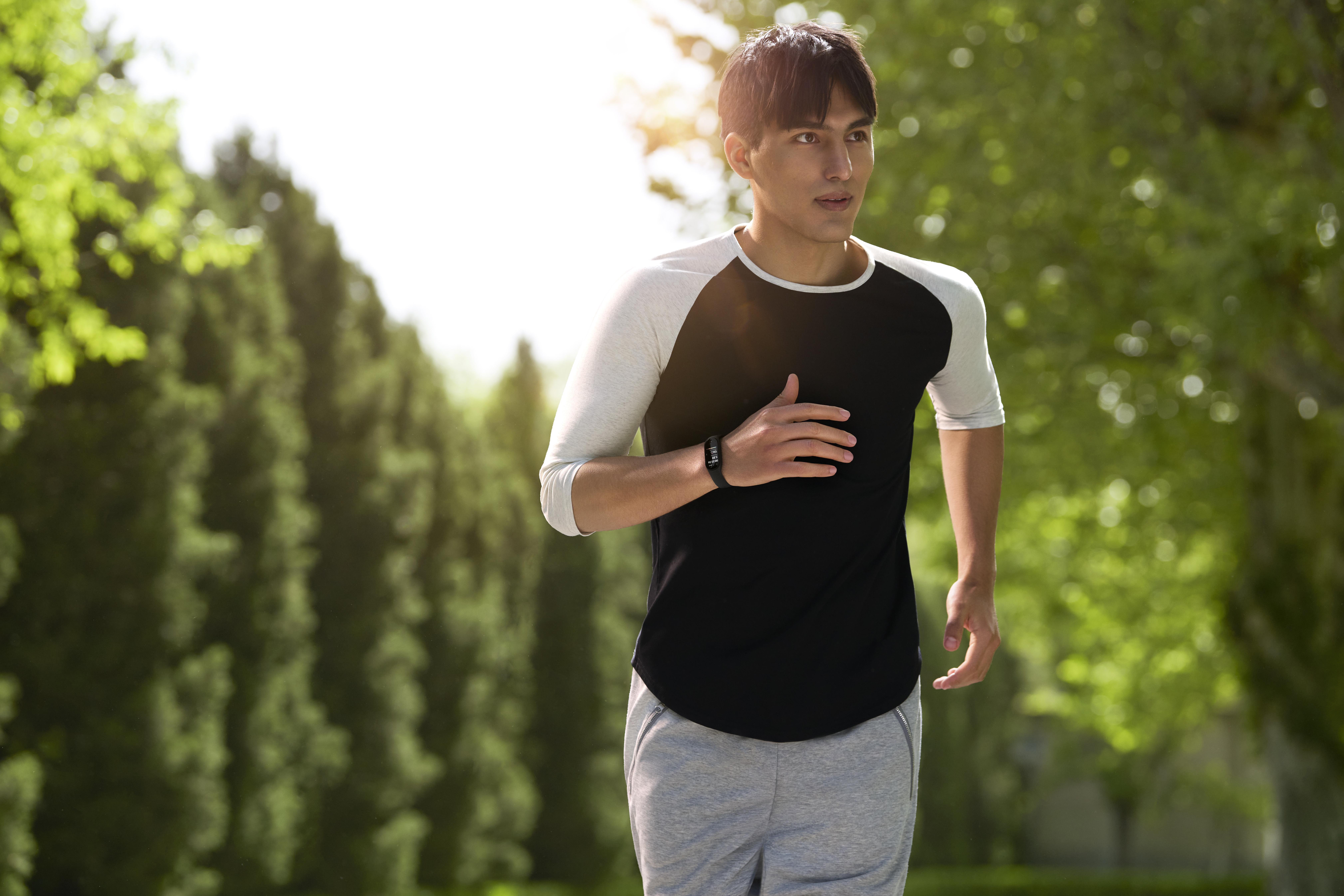 Ein Mann rennt durch einen Park, trägt ein schwarz-graues Shirt und einen Fitnesstracker.
