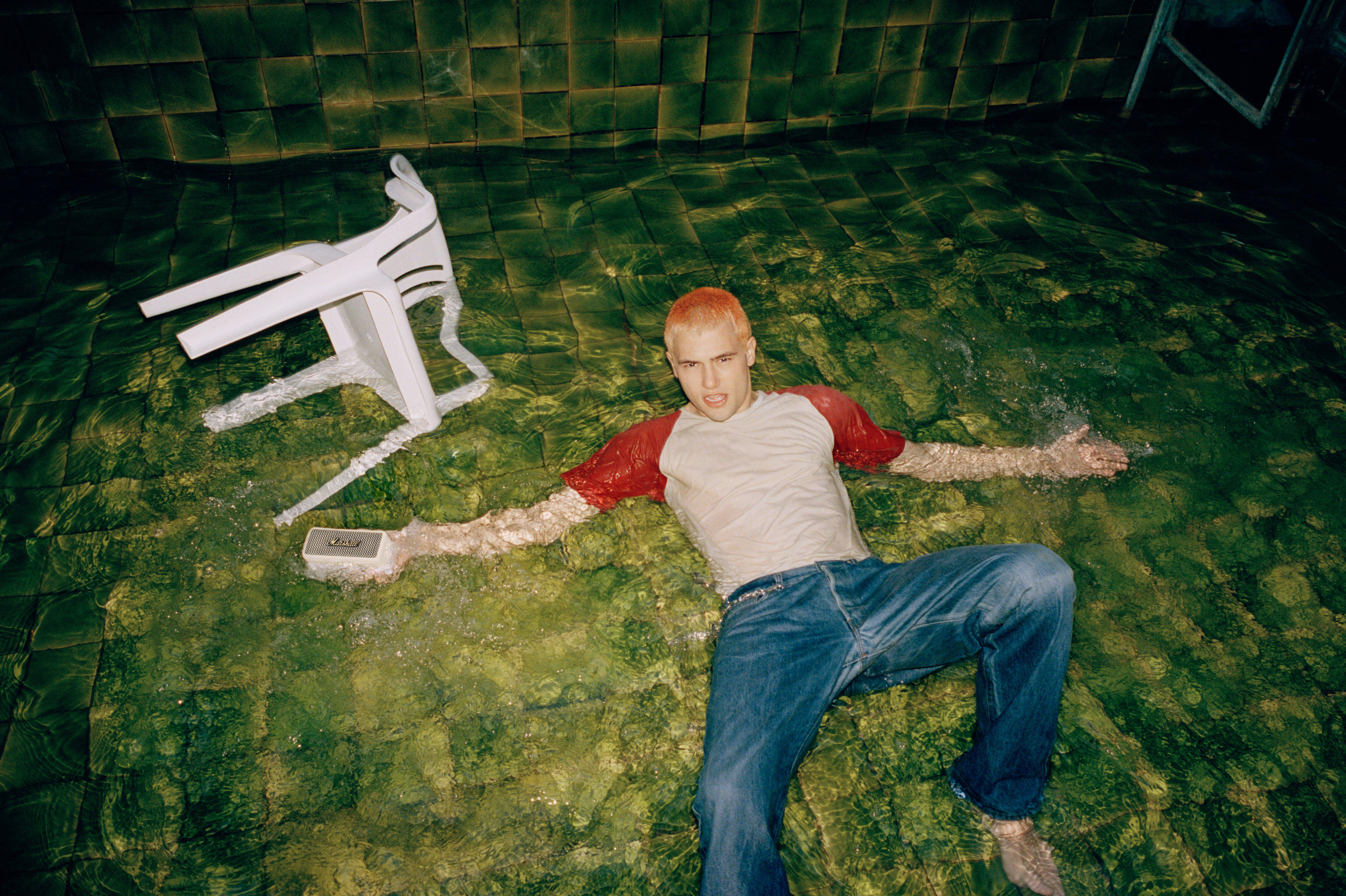 Mann im Wasser, rotes Shirt, orange Haare, Stuhl schwimmt.