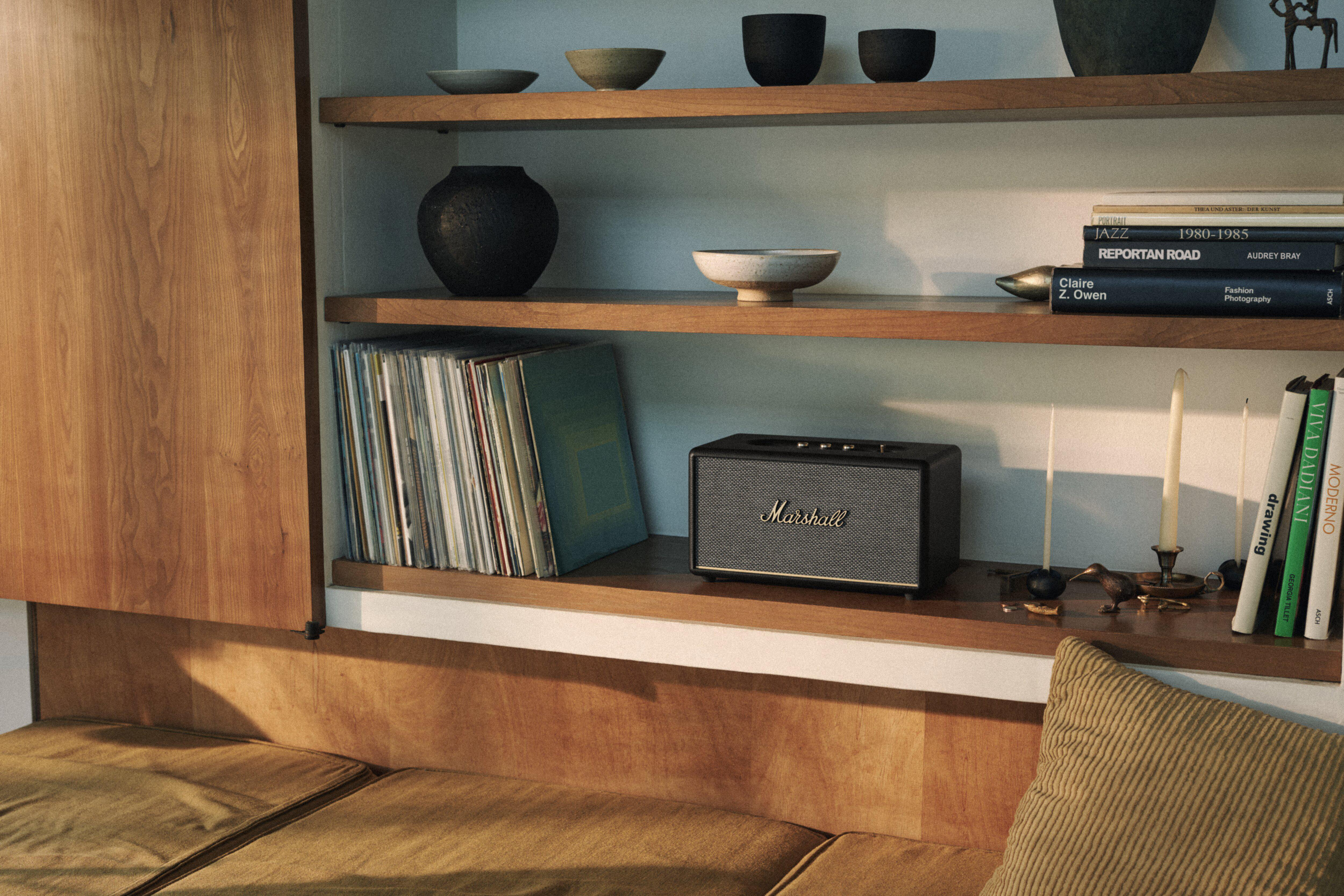 Holzregale mit Büchern, Schallplatten, einem Lautsprecher und dekorativen Schalen und Vasen. Ein Sofa ist im Vordergrund.