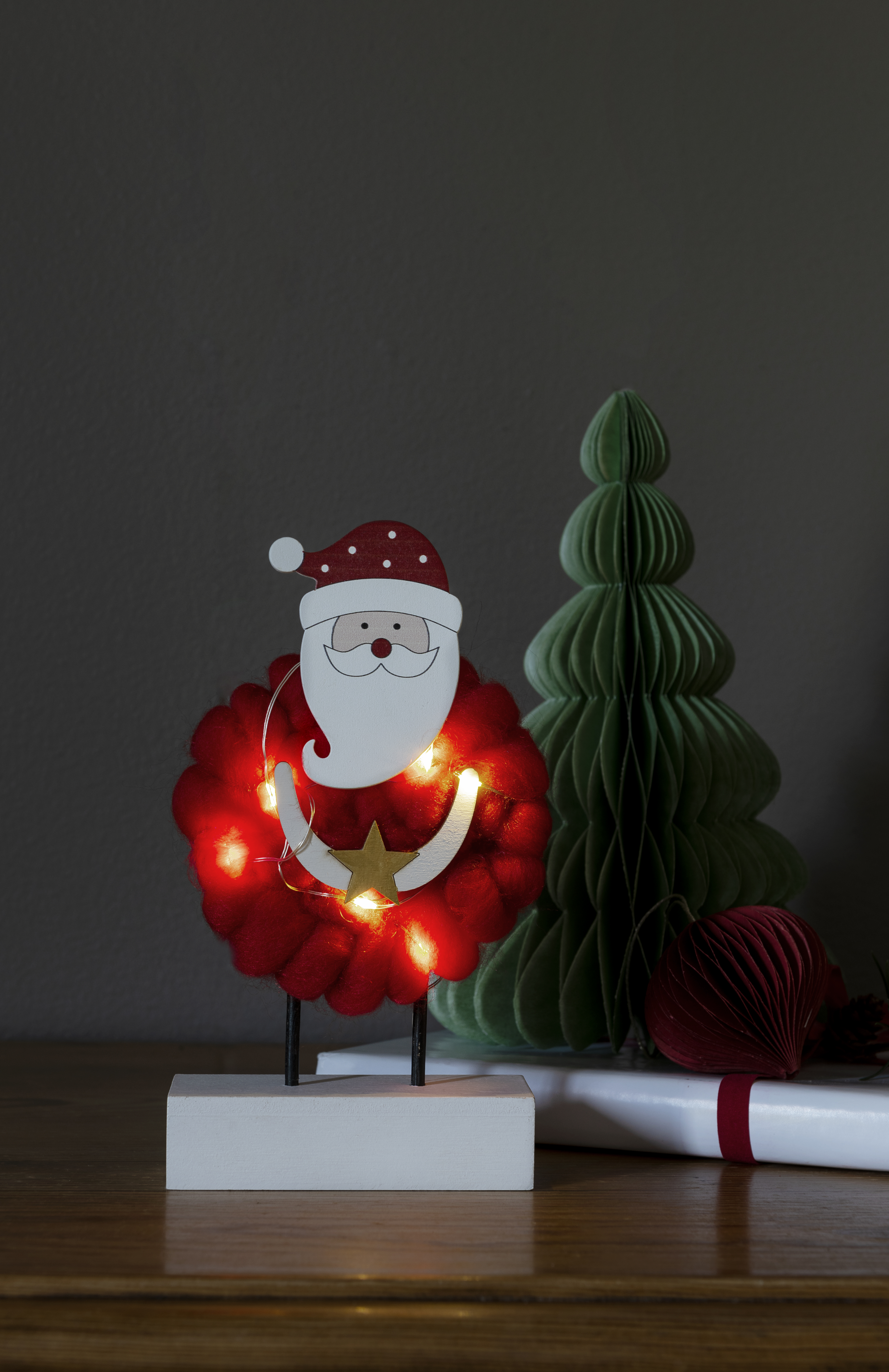 Weihnachtsdekoration mit einer Weihnachtsmannfigur, einem grünen Baum und einem roten Ornament.
