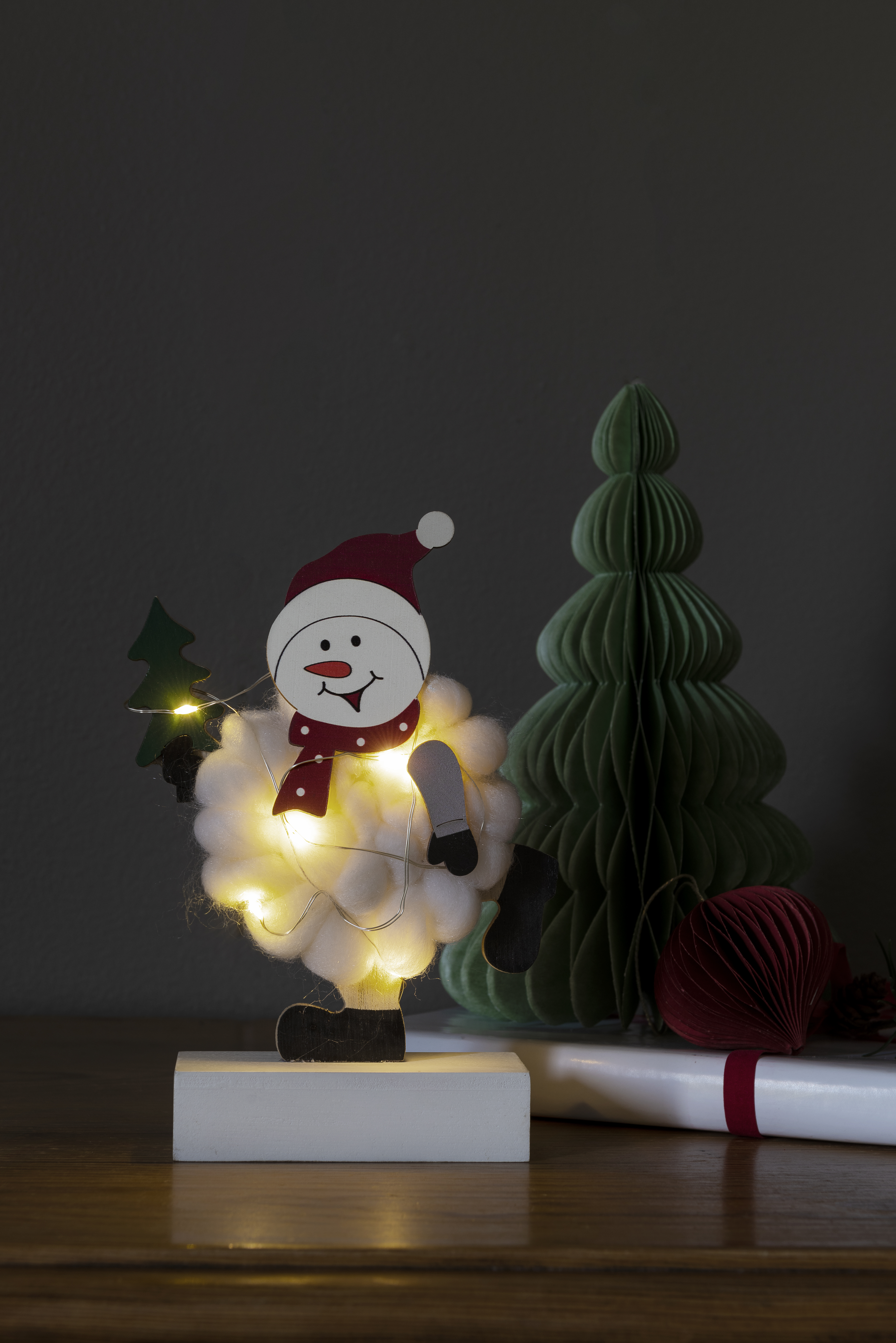 Schneemann-Dekoration mit Lichtern, ein grüner Baum und ein rotes Geschenk.