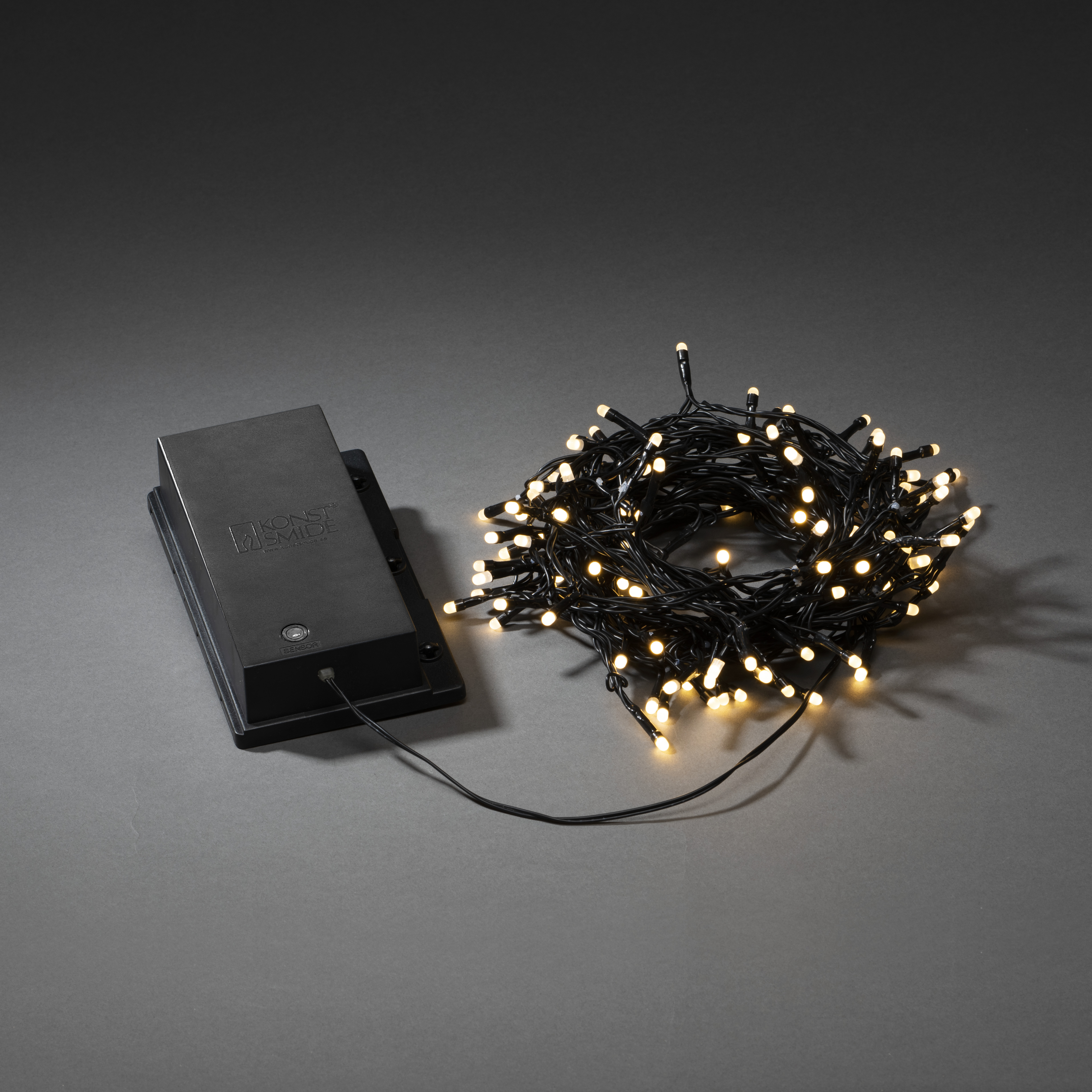 Lichterkette mit warmweißen Lichtern. Links eine schwarze Box. Lichter auf grauem Hintergrund.
