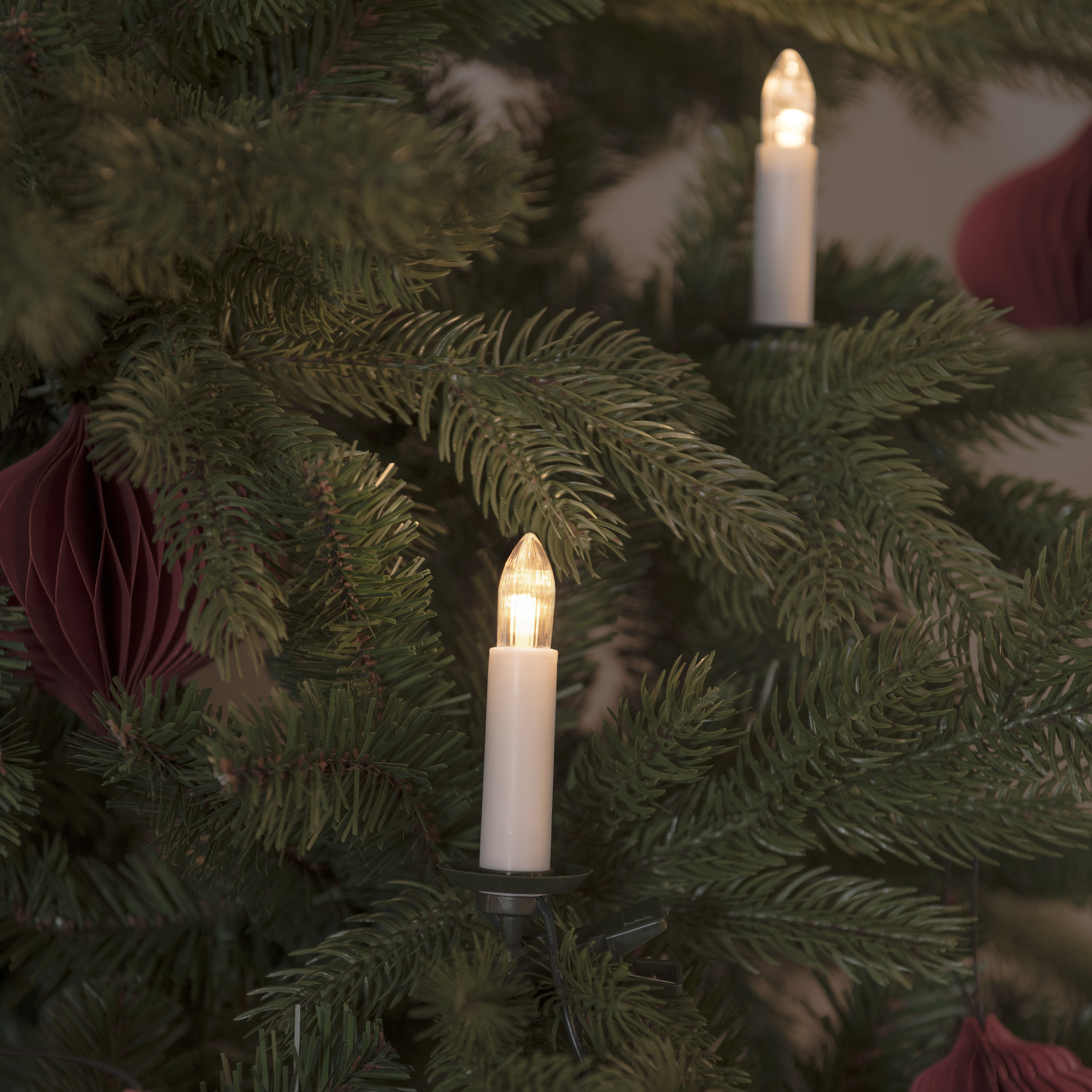 Weihnachtsbaum mit Lichtern und Ornamenten, Kerzen und roten Papierdekorationen.