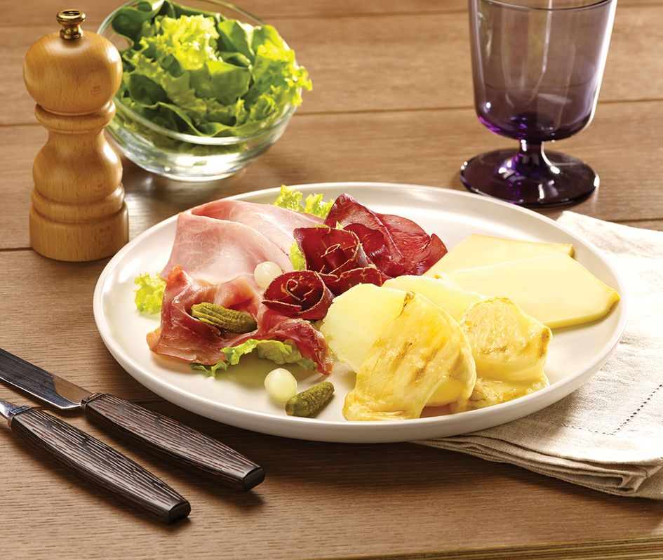 A plate of charcuterie with cheese, meat, pickles, and salad on a wooden table.