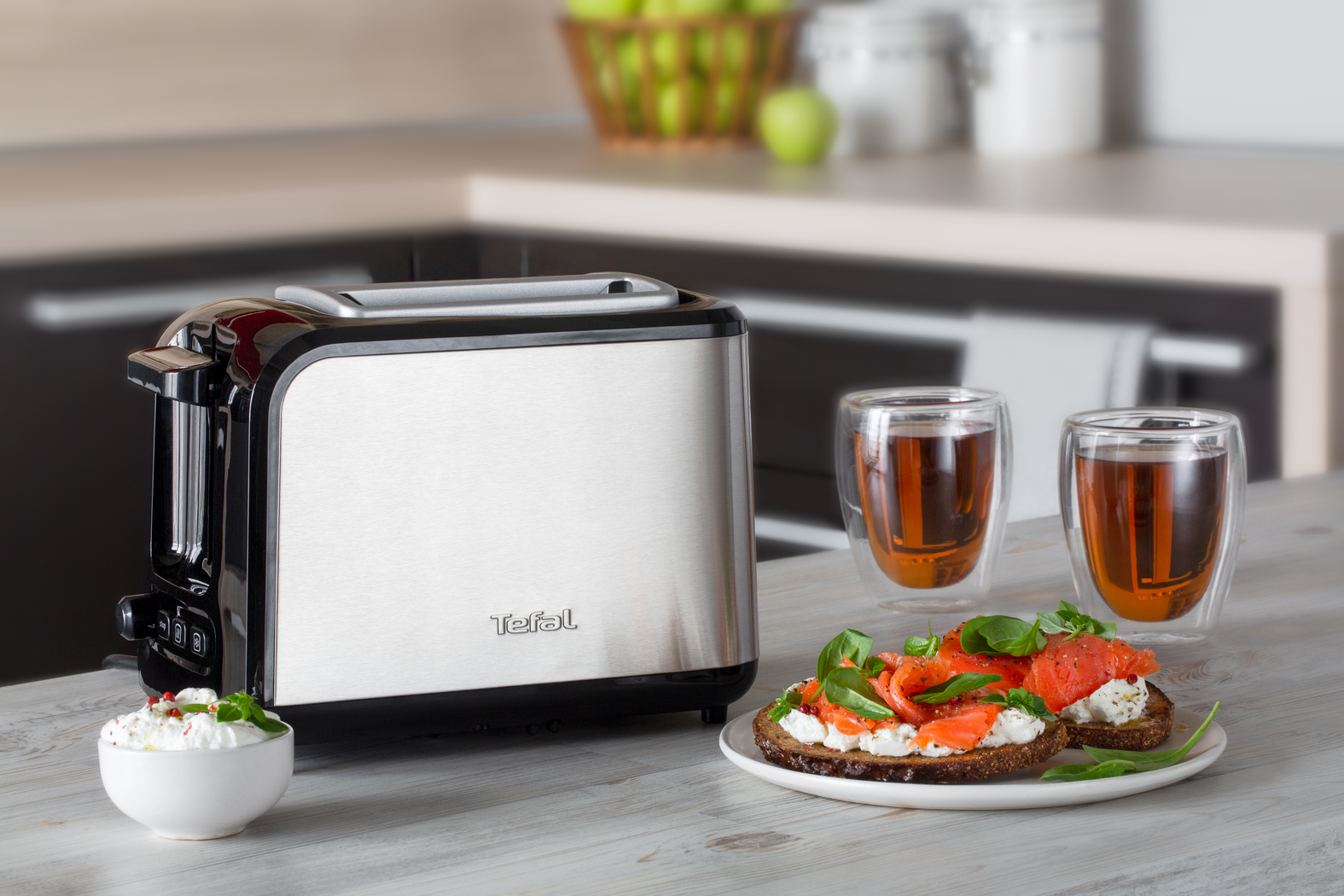 Zilveren broodrooster met toast, zalm en theekopjes op een tafel.