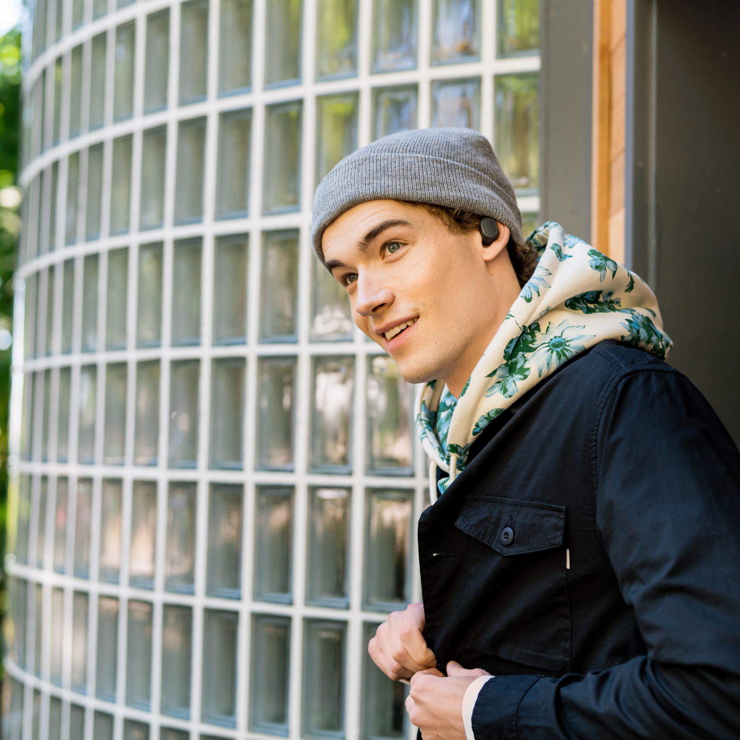 Young man with gray beanie smiles, wearing earbuds.