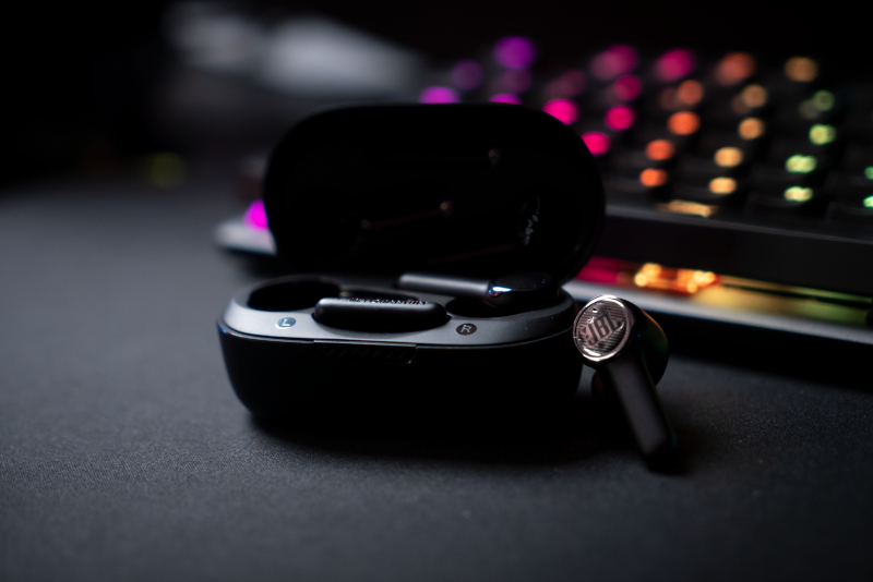 Schwarze Ohrhörer in ihrem Ladecase. Eine Tastatur ist im Hintergrund.
