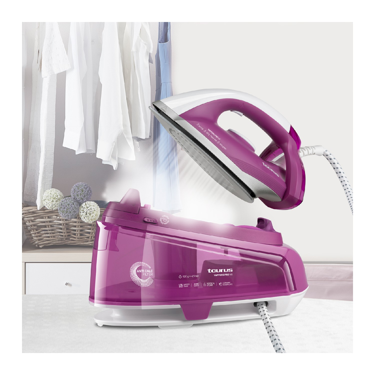 Una plancha de vapor rosa y blanca se encuentra encima de su base rosa. Ropa colgada detrás.
