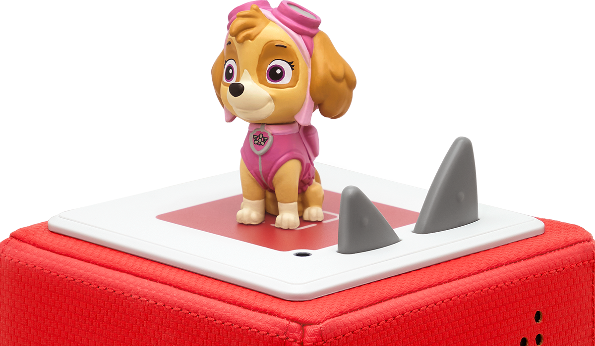 Eine Skye-Figur von Paw Patrol auf einer roten Plattform mit Haifischflossen-Dekoration, schwarzer Hintergrund.