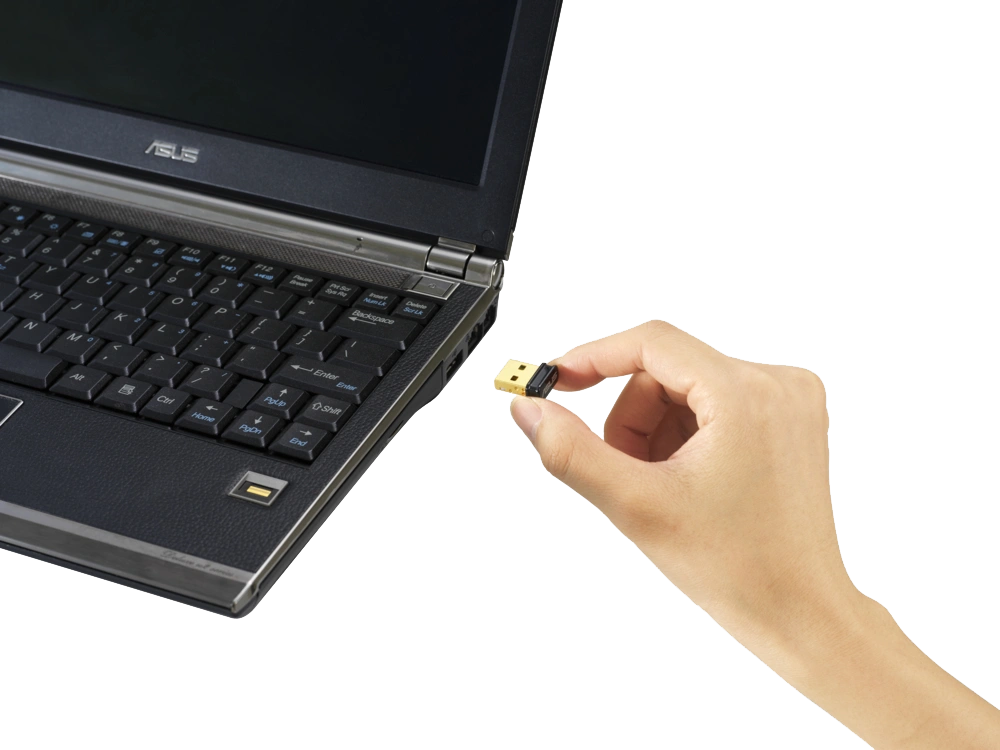 A hand holding a USB dongle next to a laptop keyboard.