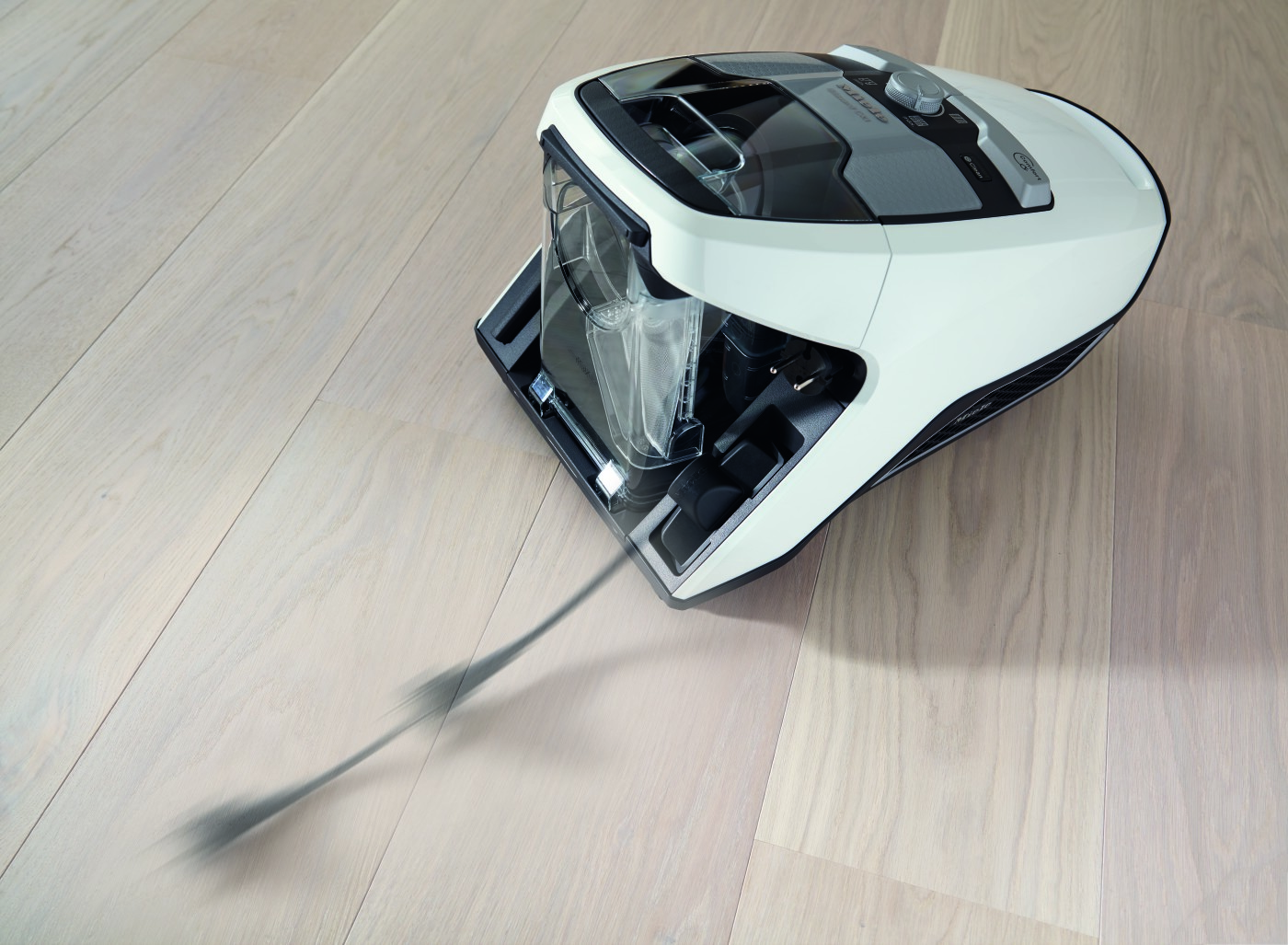 White vacuum cleaner on a wooden floor, open dust container.