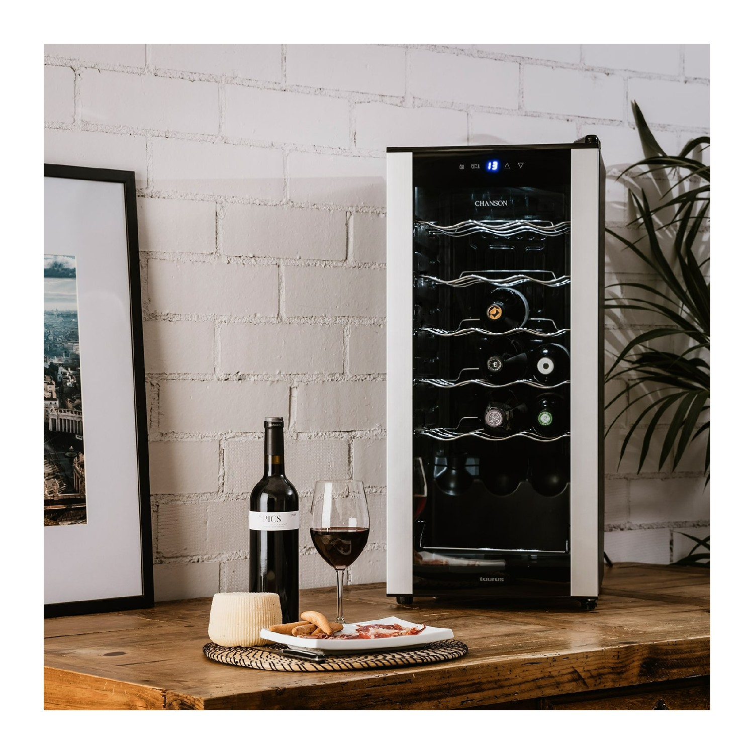 Vinoteca con botellas, una copa de vino y un plato de queso sobre una mesa de madera, con pared de ladrillo.