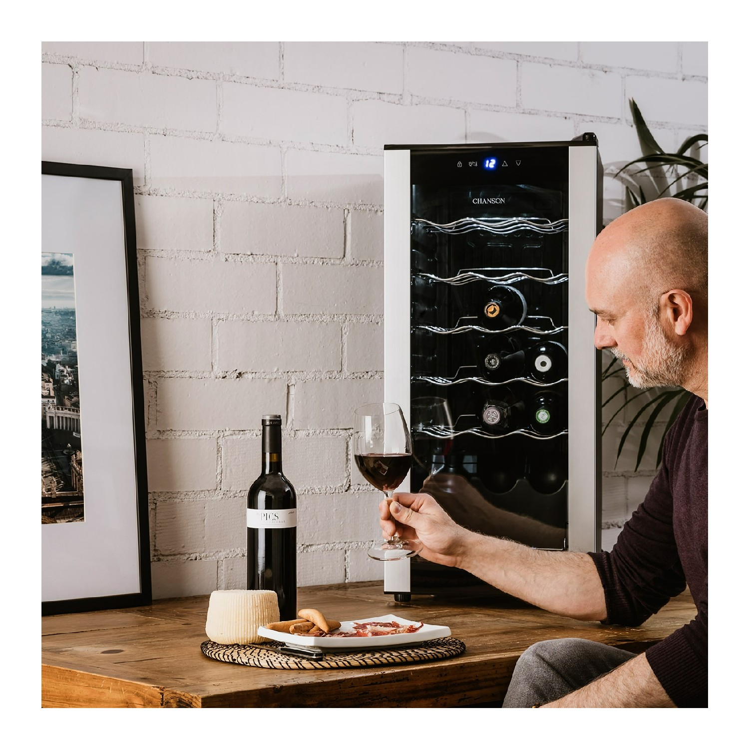 Un hombre sosteniendo una copa de vino tinto, junto a una vinoteca con botellas.