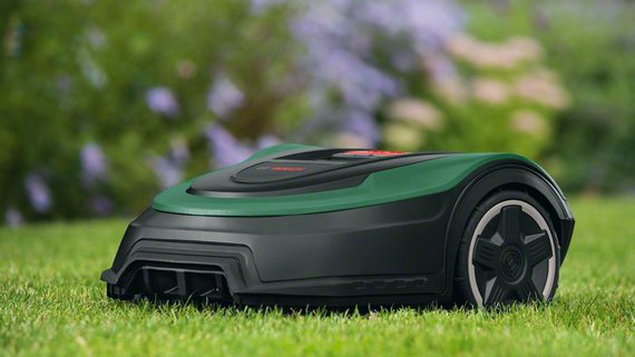 Robotfűnyíró a füvön, zöld és fekete. Zöld fű és elmosódott zöld háttér.