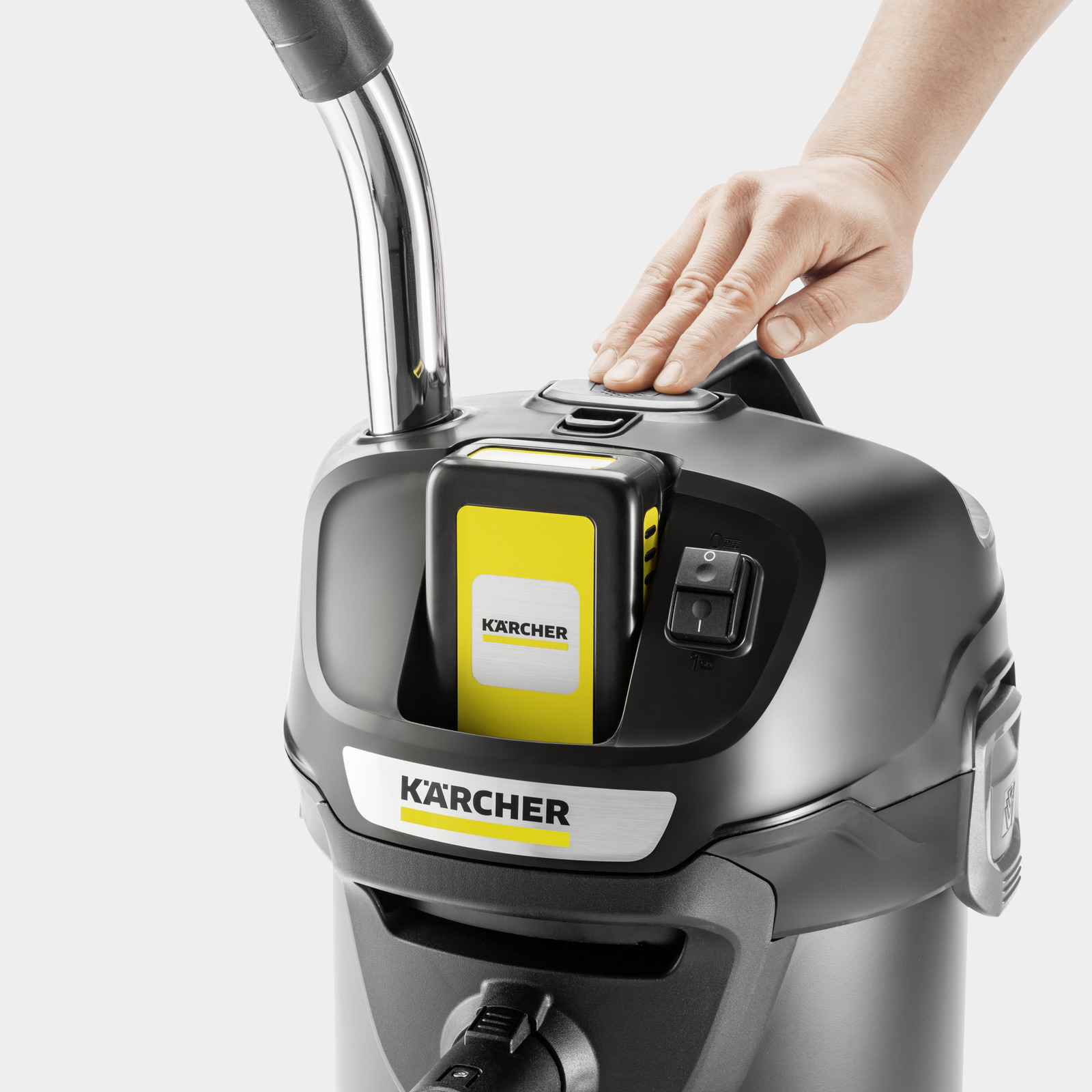 Egy kéz megnyomja a bekapcsológombot egy Karcher porszívón. Sárga akkumulátor látható.