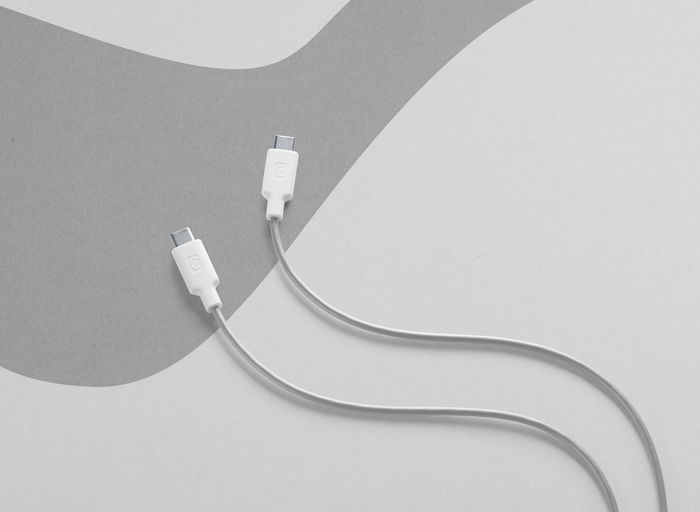 Dos cables USB-C blancos con conectores blancos sobre fondo gris y blanco.