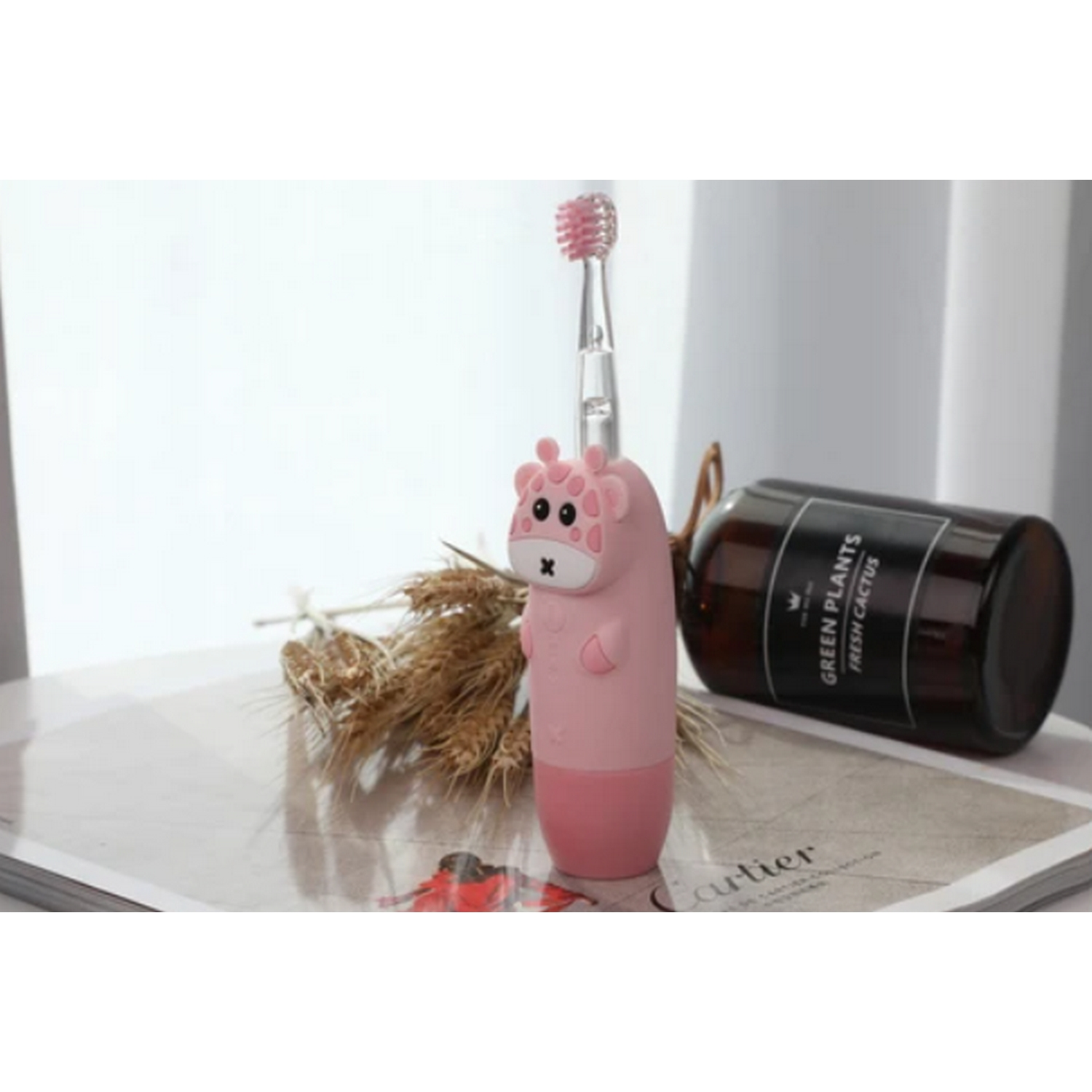 Un cepillo de dientes y soporte de jirafa rosa en una revista, con una botella de cactus.