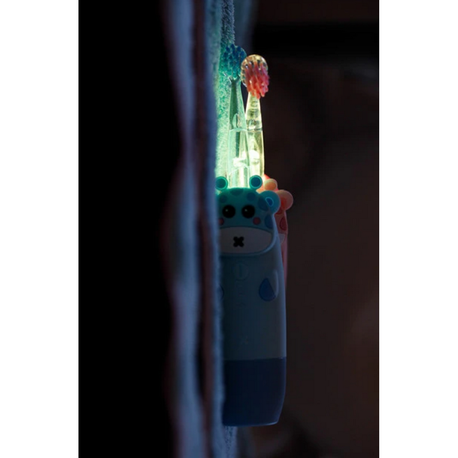 Se muestra un cepillo de dientes azul con una cabeza en forma de jirafa en una habitación oscura.