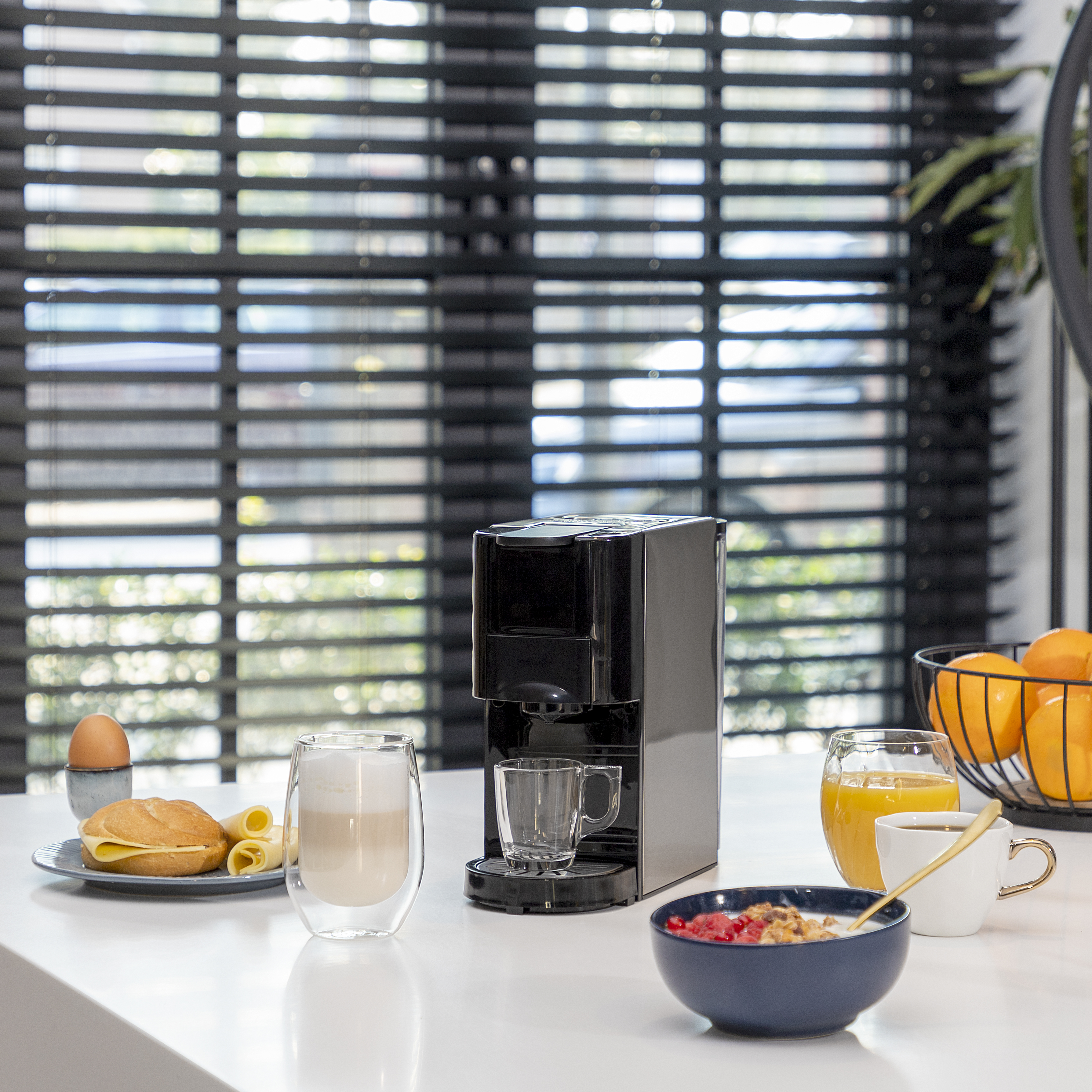 Ontbijt met koffiezetapparaat, koffiekopjes, ei, brood en fruit. Fel daglicht op de achtergrond.