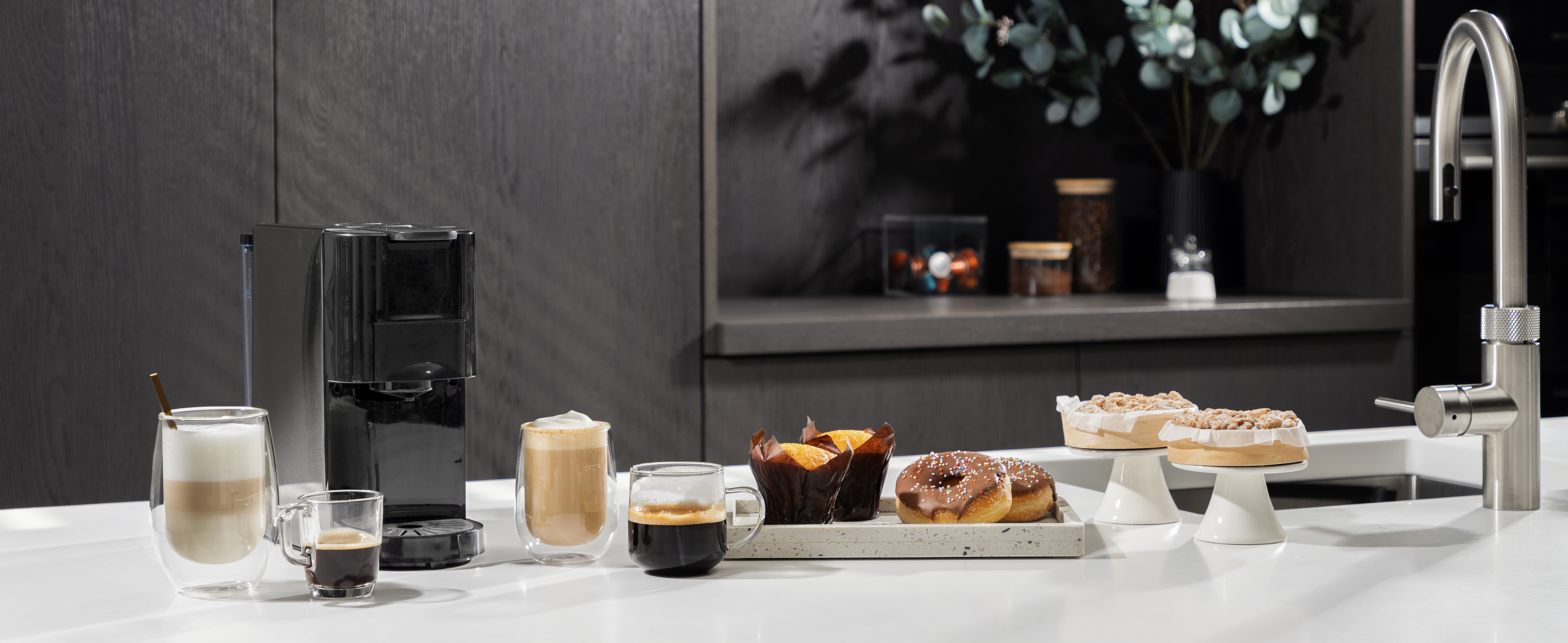 Keukenblad met koffiezetapparaat, koffie, muffins en donuts tentoongesteld.